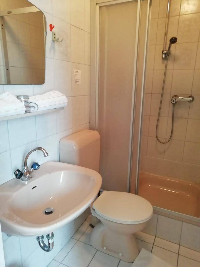 Kleines Badezimmer mit Dusche, WC, Waschbecken und beigefarbenen Fliesen.