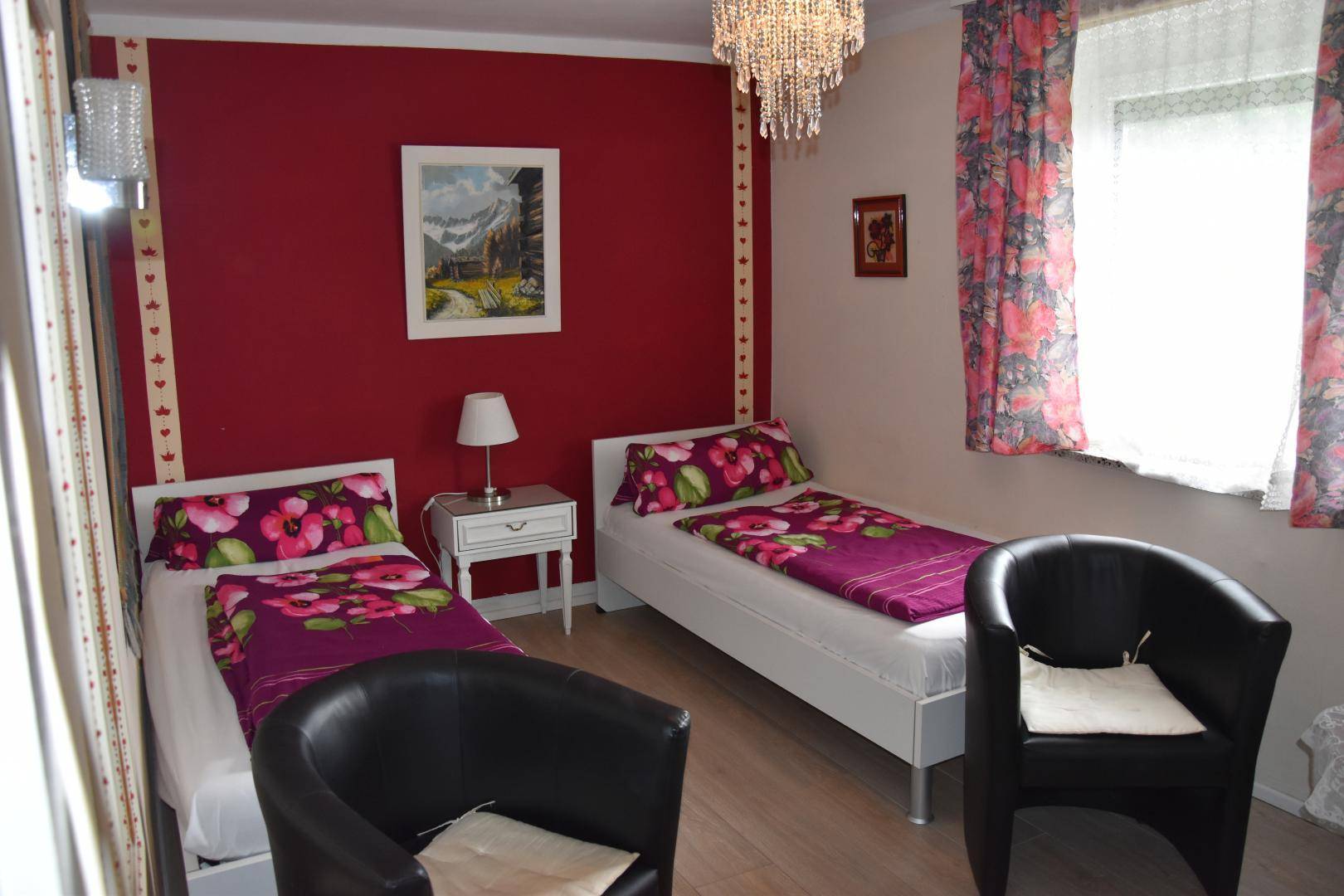 Schlafzimmer mit zwei Einzelbetten, roten Wänden und floralen Bettbezügen.