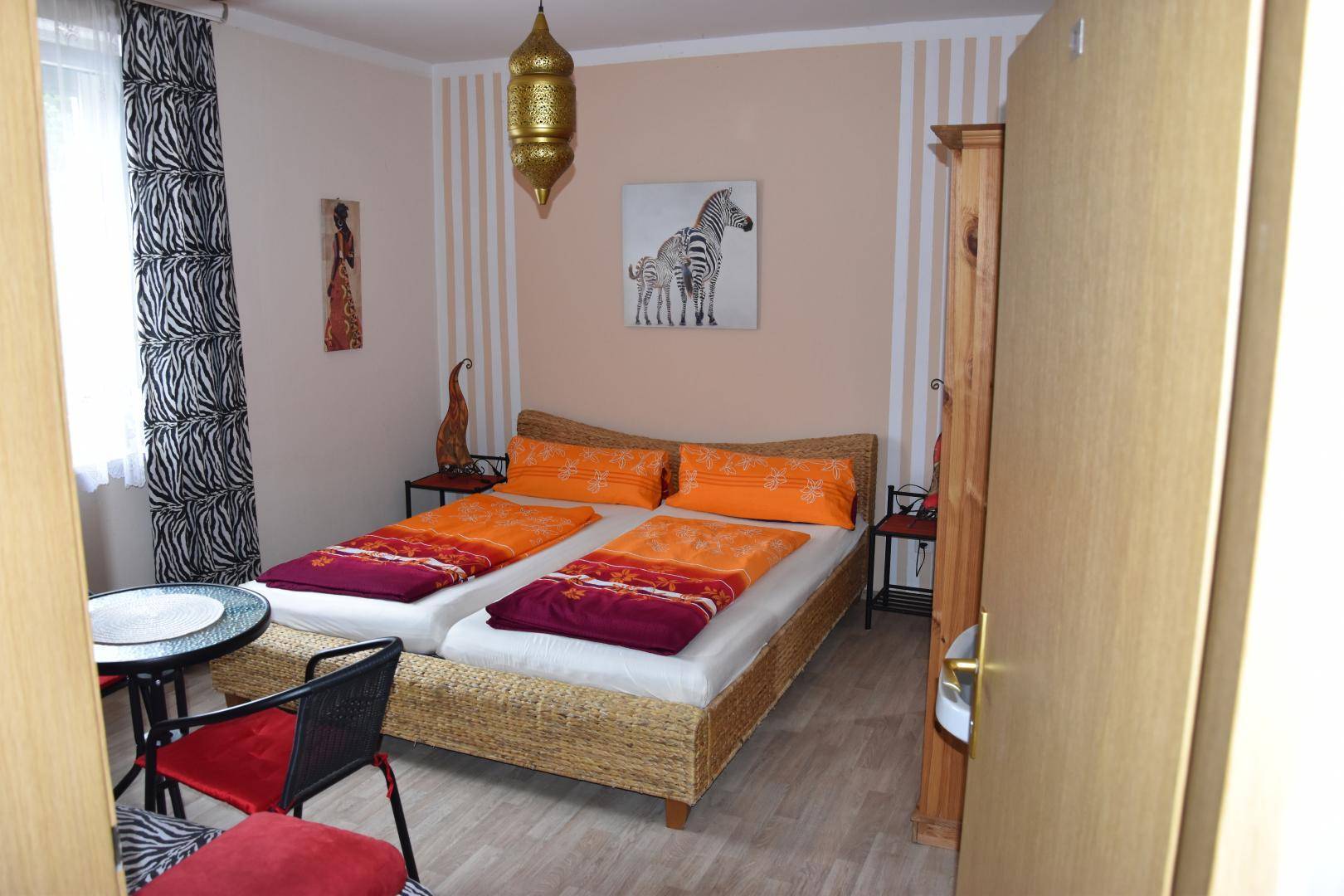 Gemütliches Schlafzimmer mit Doppelbett, afrikanisch inspirierten Vorhängen und Laternenlampe.