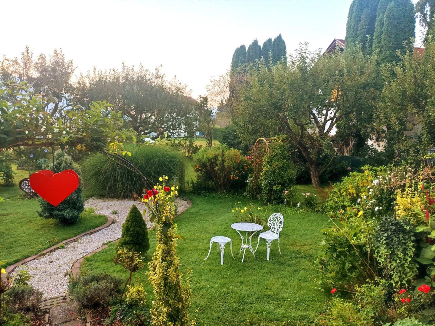 Romantischer Gartenweg mit Kies, Blumenbeeten und einer kleinen, charmanten Sitzecke.