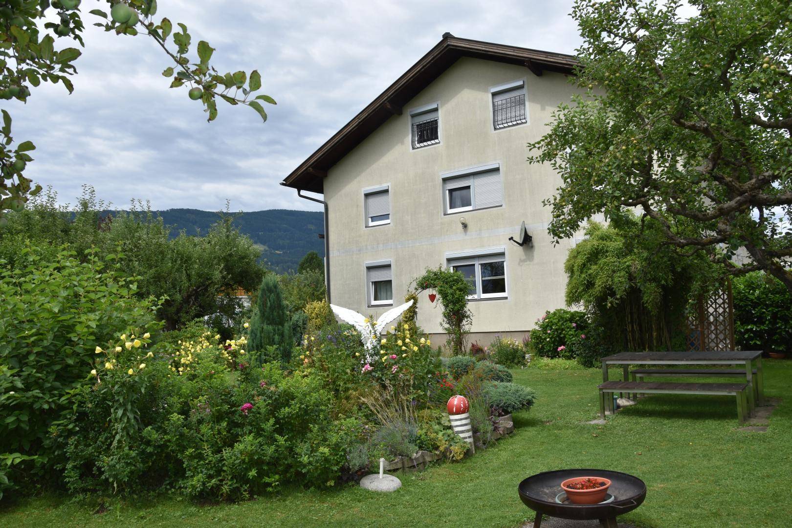 Idyllischer Gartenbereich hinter dem Haus mit Sitzbank, Blumenbeeten und Feuerstelle.