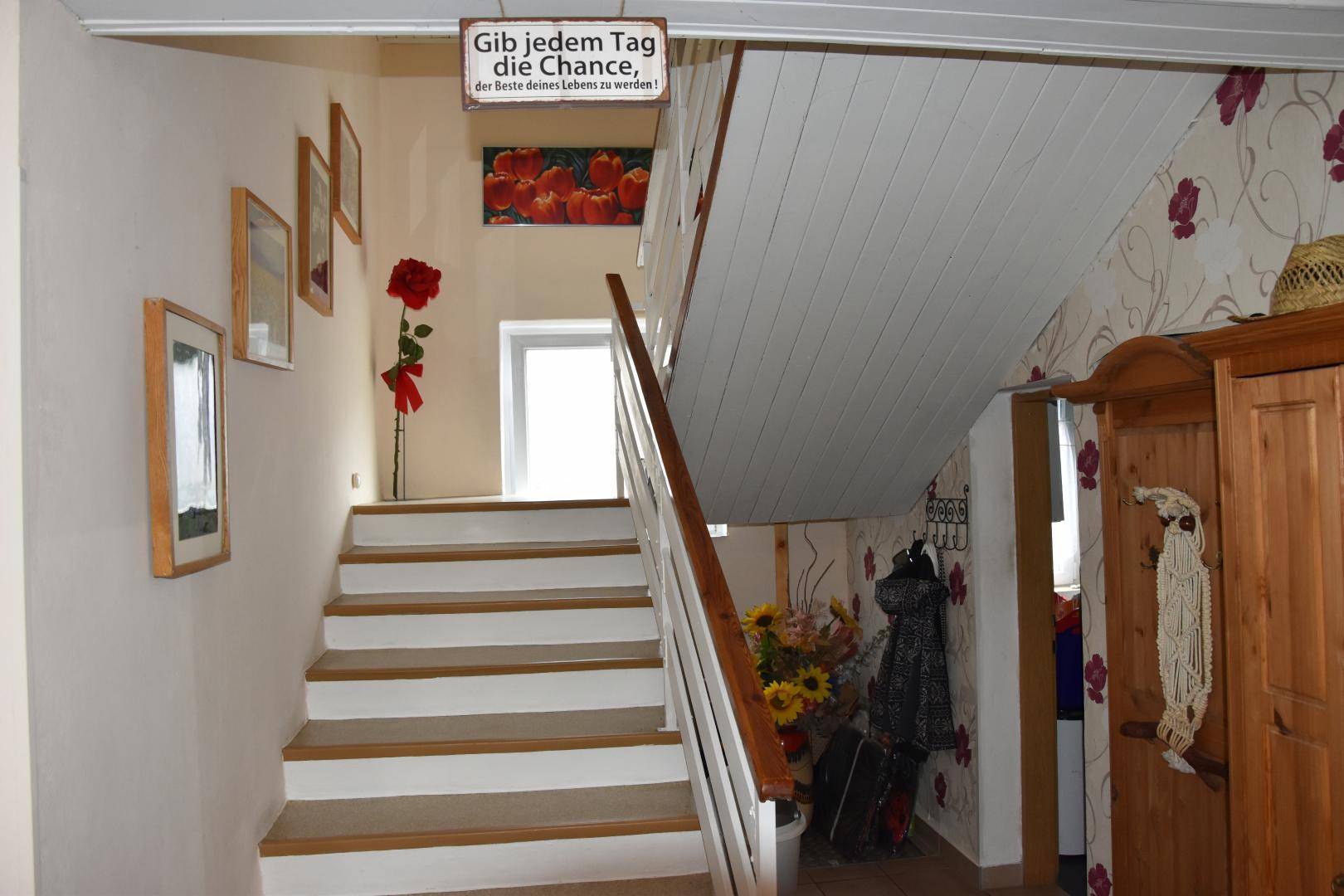 Treppenhaus mit Holzstufen, weißem Geländer und dekorativer Tapete.