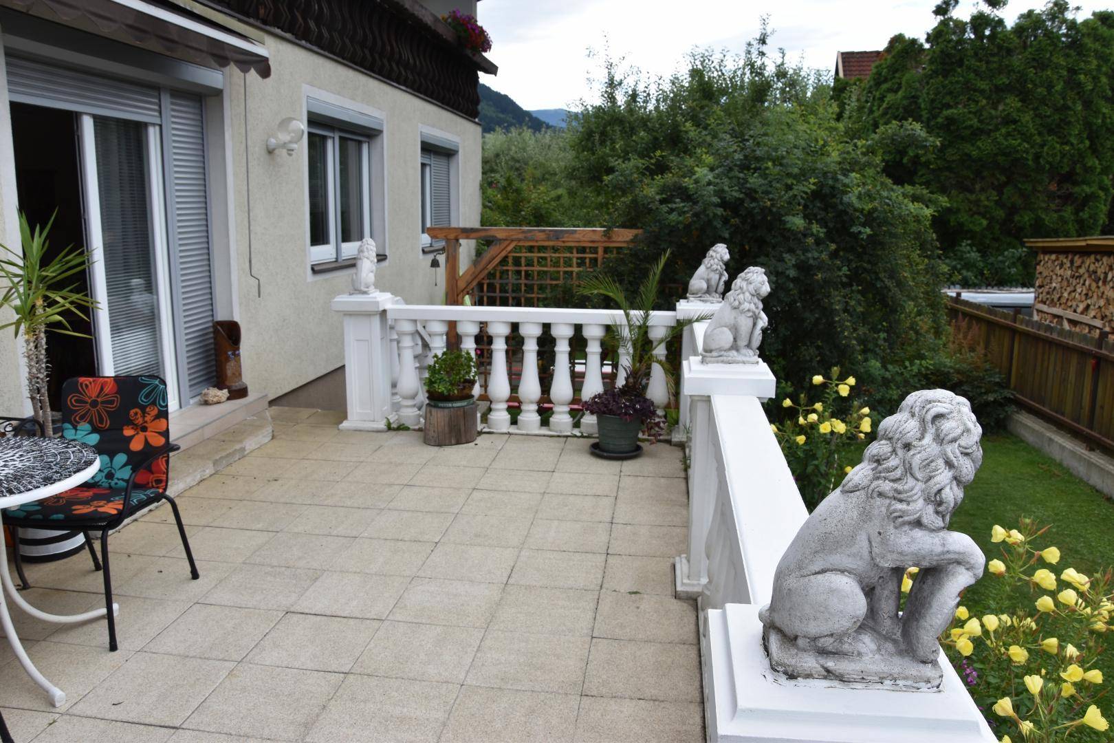 Geräumige geflieste Terrasse mit Balustrade, dekorativen Löwenstatuen und Gartenblick.