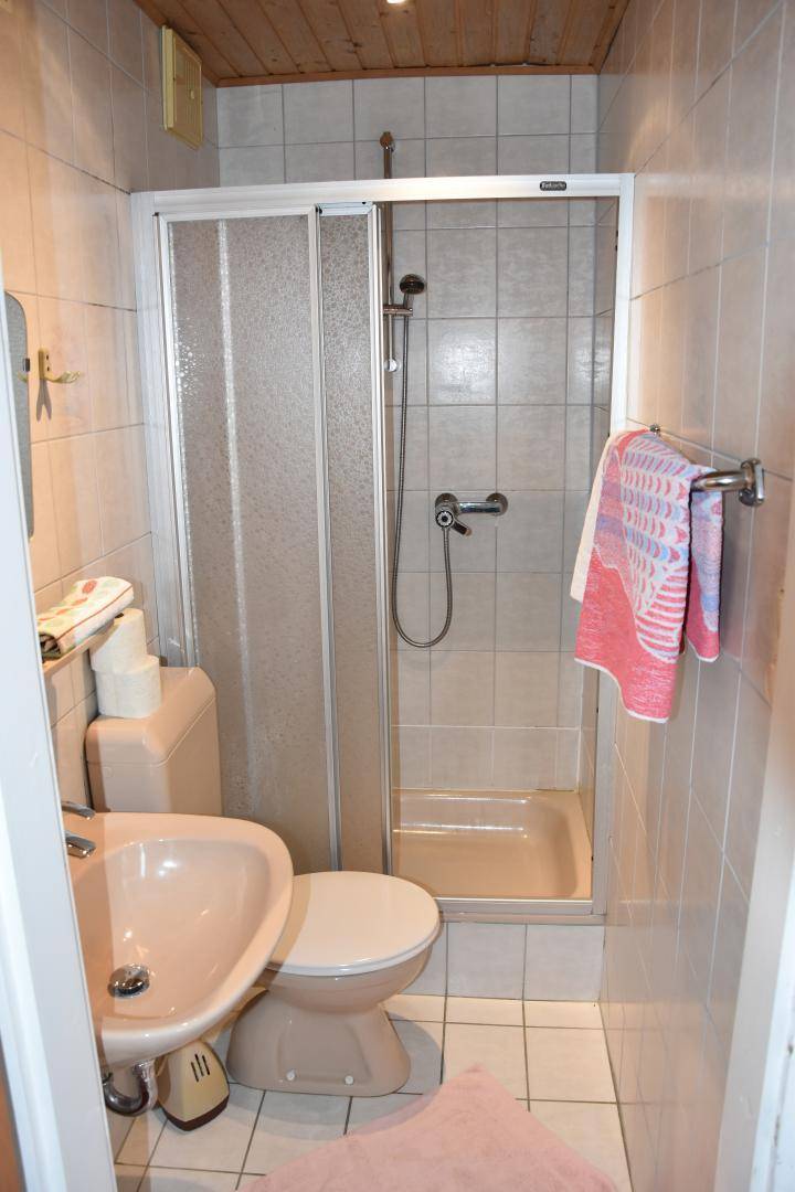 Kleines Badezimmer mit Dusche, WC, Waschbecken und beigefarbenen Fliesen.