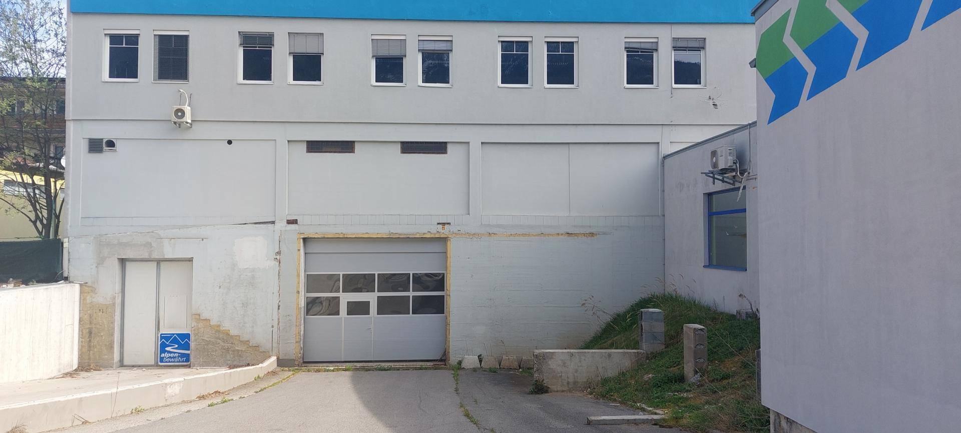 Detailansicht der Gebäudefassade mit Garagentor, Eingangstür und Fenstern im oberen Bereich.