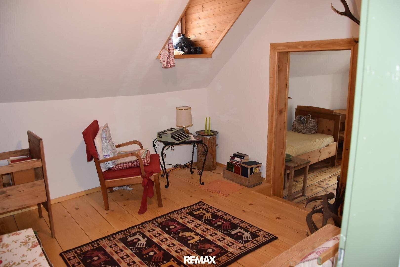 Dachzimmer mit Holzboden, Schreibtisch und gemütlichem Sessel, ideal als Arbeitsbereich.