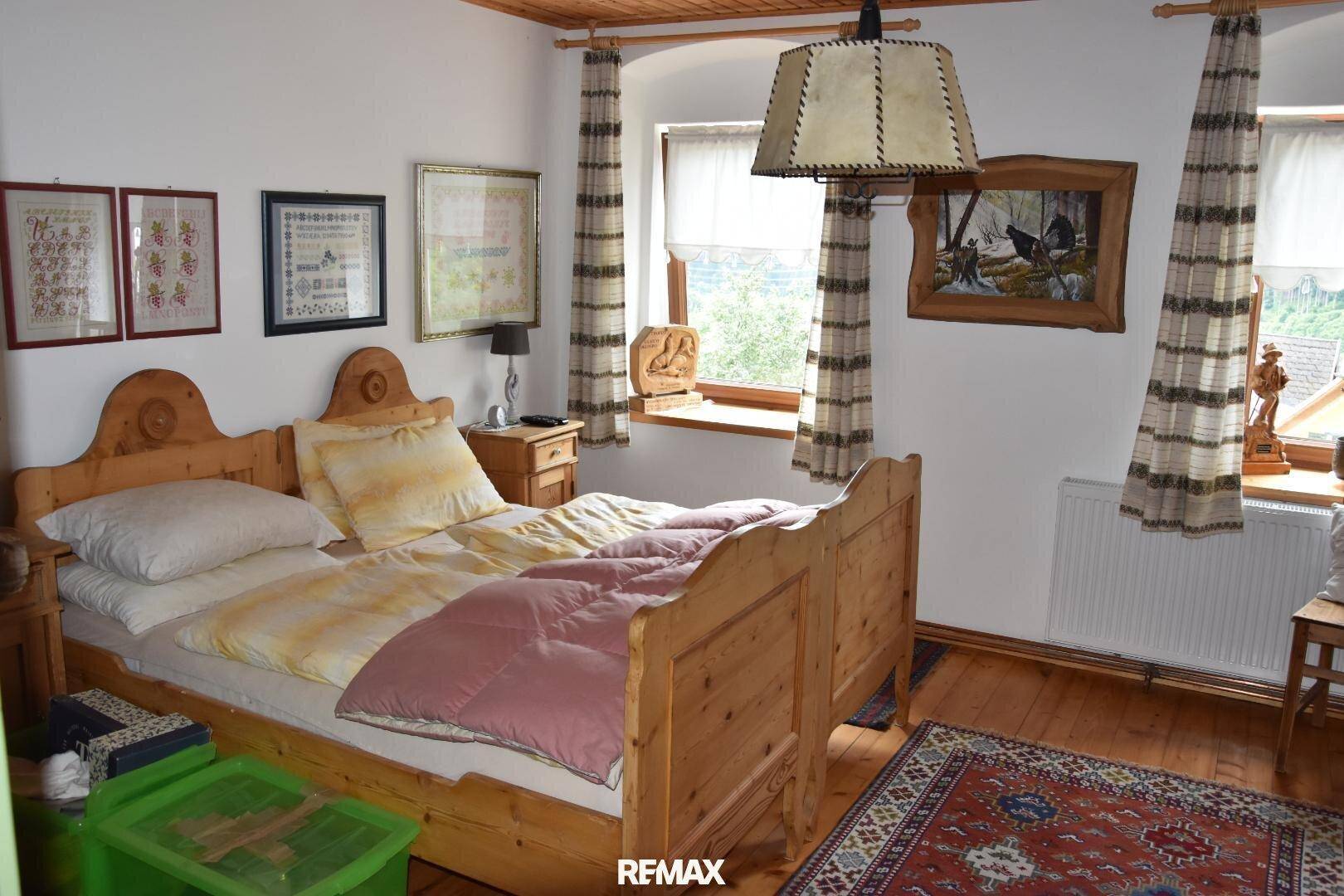 Schlafzimmer mit traditionellem Holzbett, Holzboden und karierten Vorhängen.
