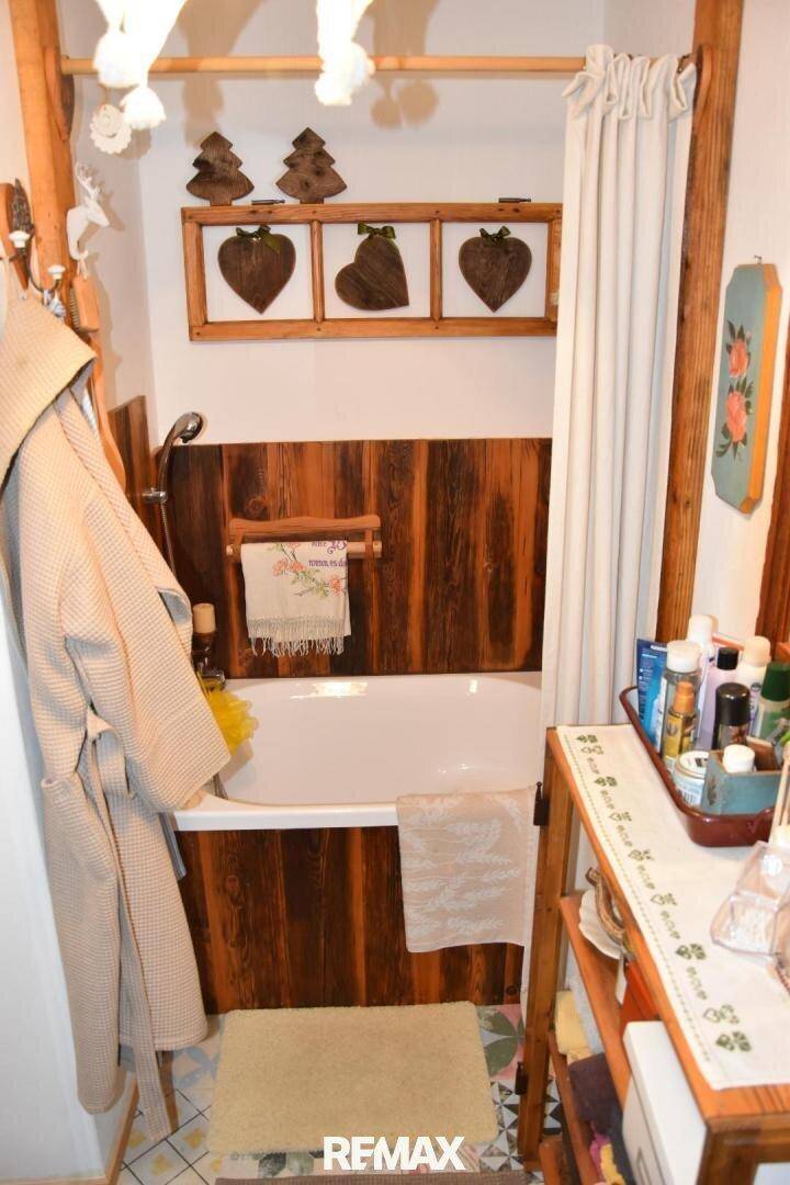 Kleines Badezimmer mit Badewanne, Holzverkleidung und rustikalen Dekorationselementen.