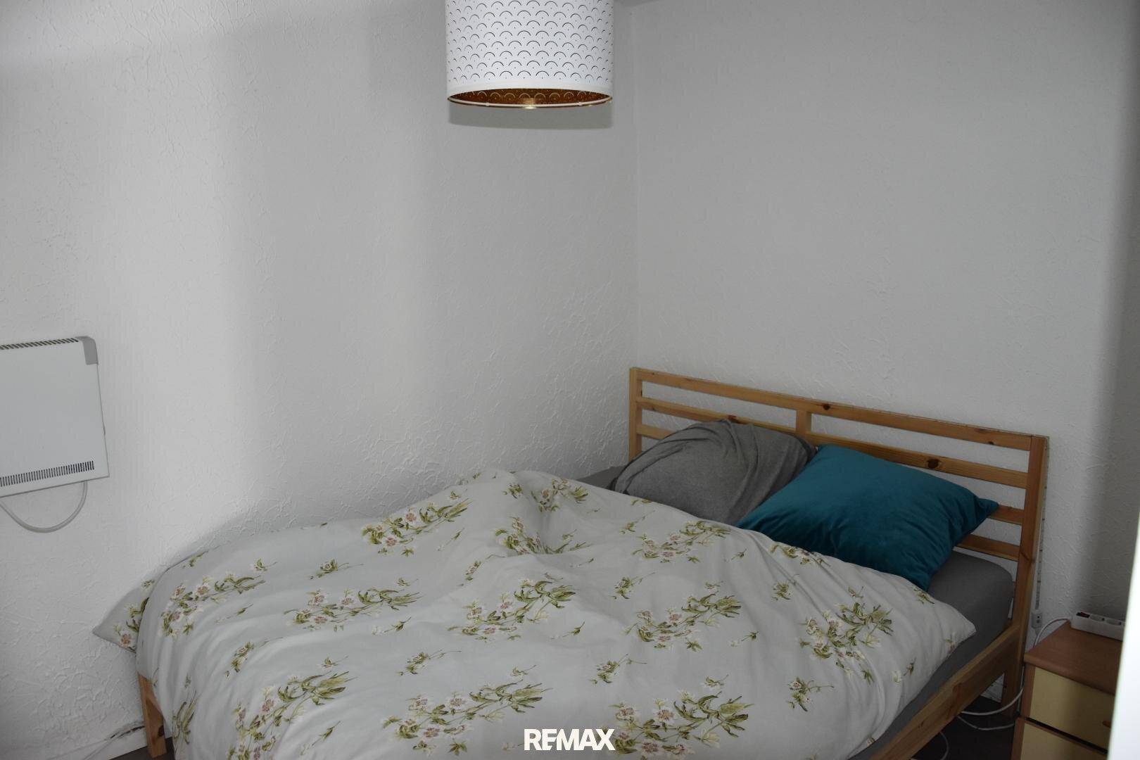 Schlafzimmer mit einem Holzbett und einer floral gemusterten Bettdecke in einem hellen Raum.