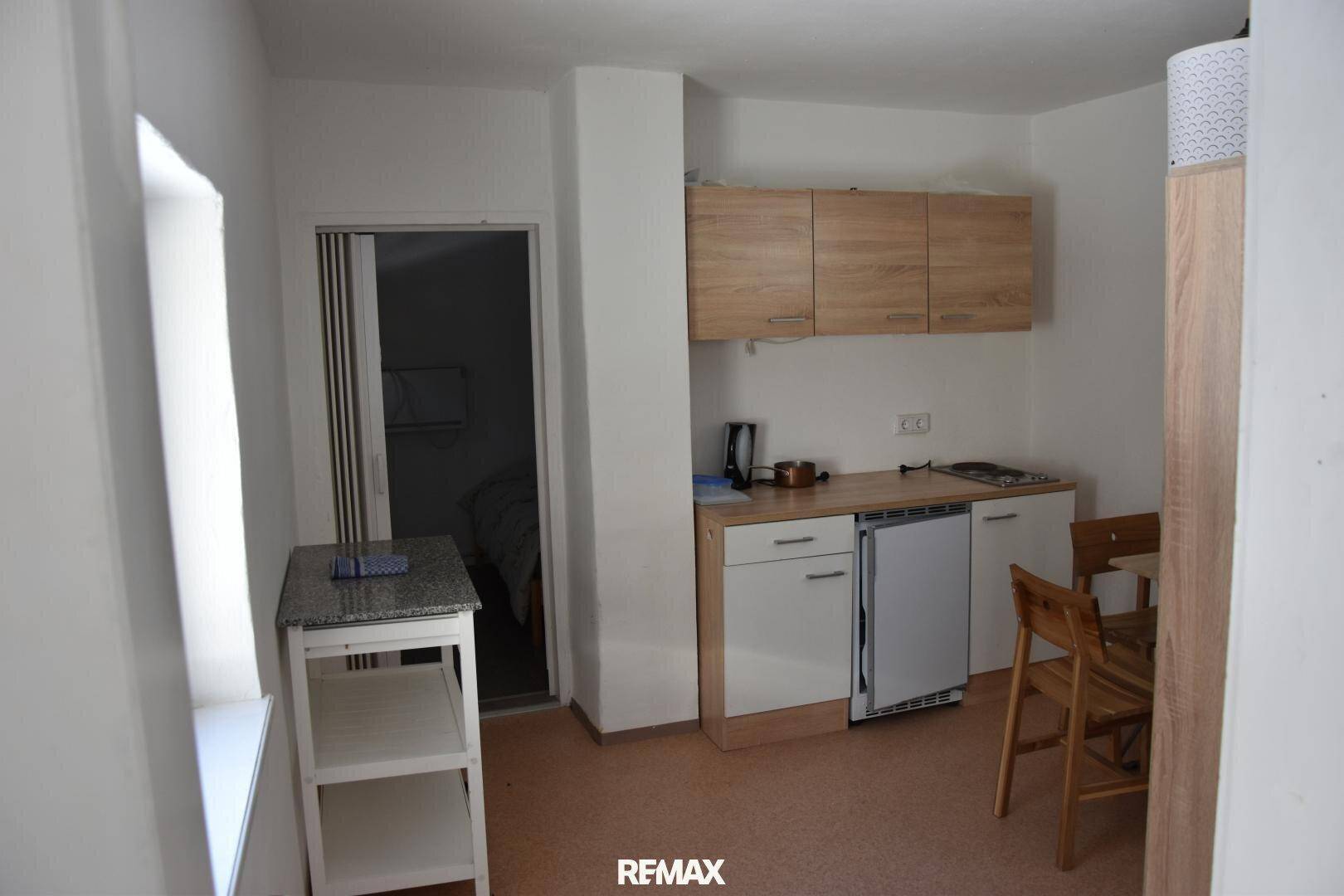 Kleine Küchenzeile mit Holzschränken, Spüle und Kühlschrank, ergänzt durch einen Esstisch mit Stühlen.