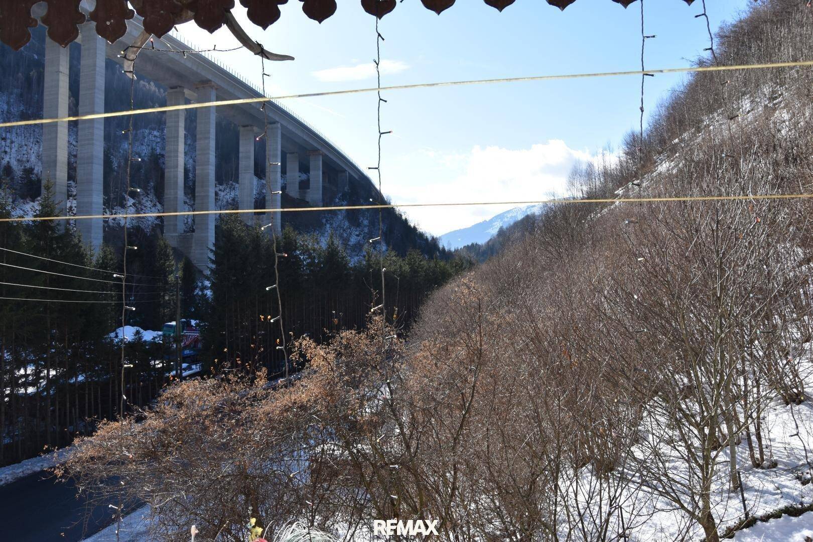 Panoramablick von einem Balkon auf eine beeindruckende Brücke, Berge und eine verschneite Landschaft.