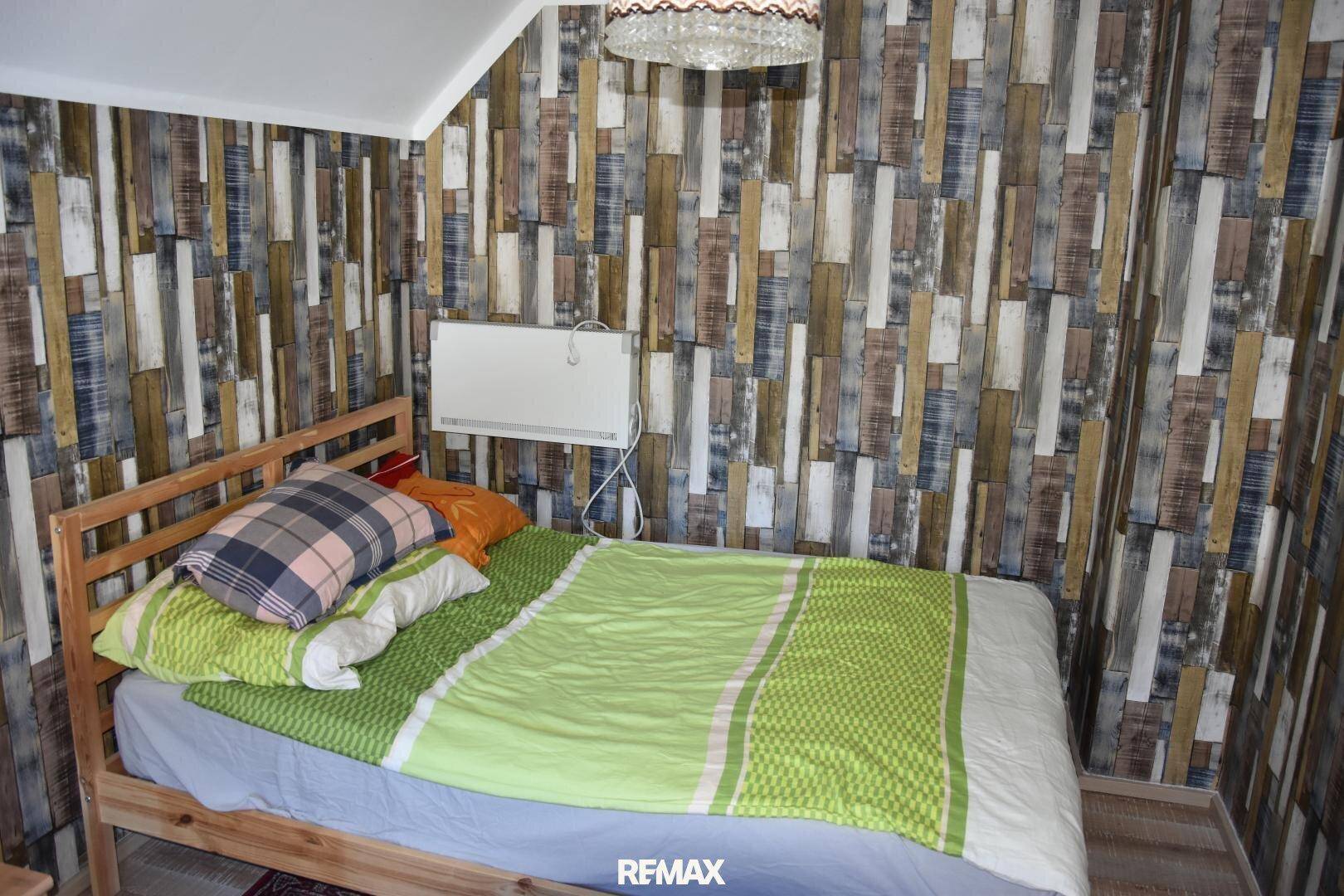 Gemütliches Schlafzimmer mit Holzbett, grüner Bettwäsche und einer Wand mit Holzoptik-Tapete.
