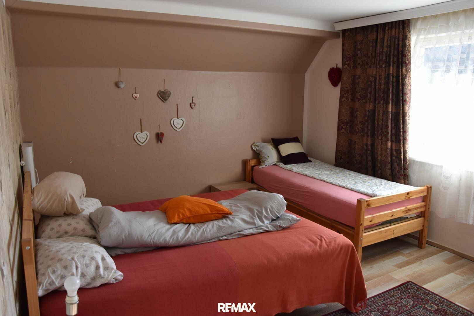 Schlafzimmer mit zwei Einzelbetten, braunen Wänden und einem Fenster, das den Raum erhellt.