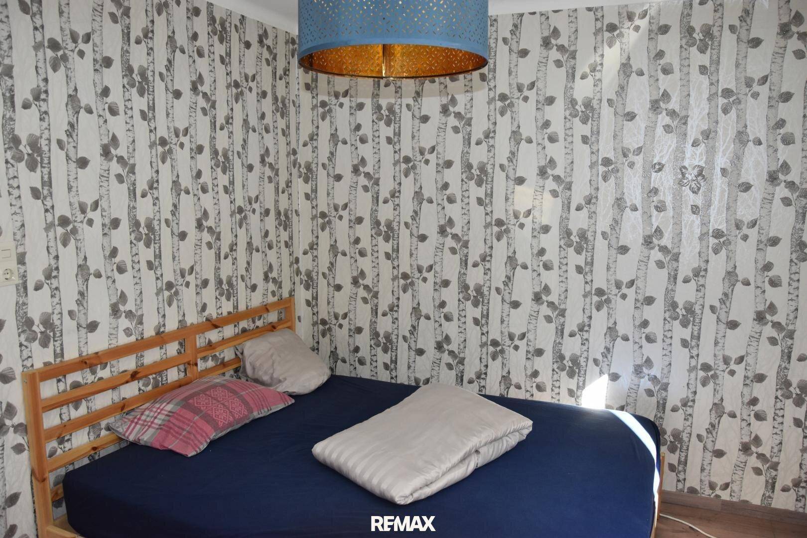 Helles Schlafzimmer mit gemusterter Tapete, einem Holzbett und einem dekorativen Deckenlicht.