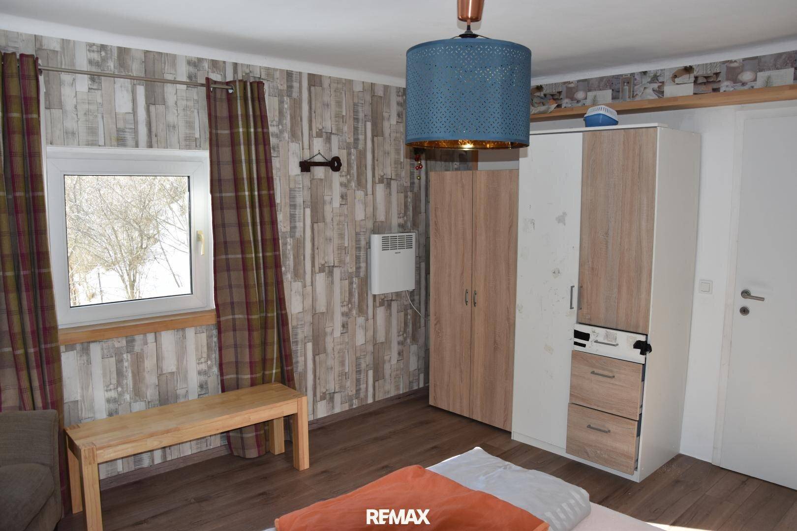 Schlafzimmer mit Holzboden, einem Kleiderschrank und zwei Fenstern, die den Raum mit Licht füllen.
