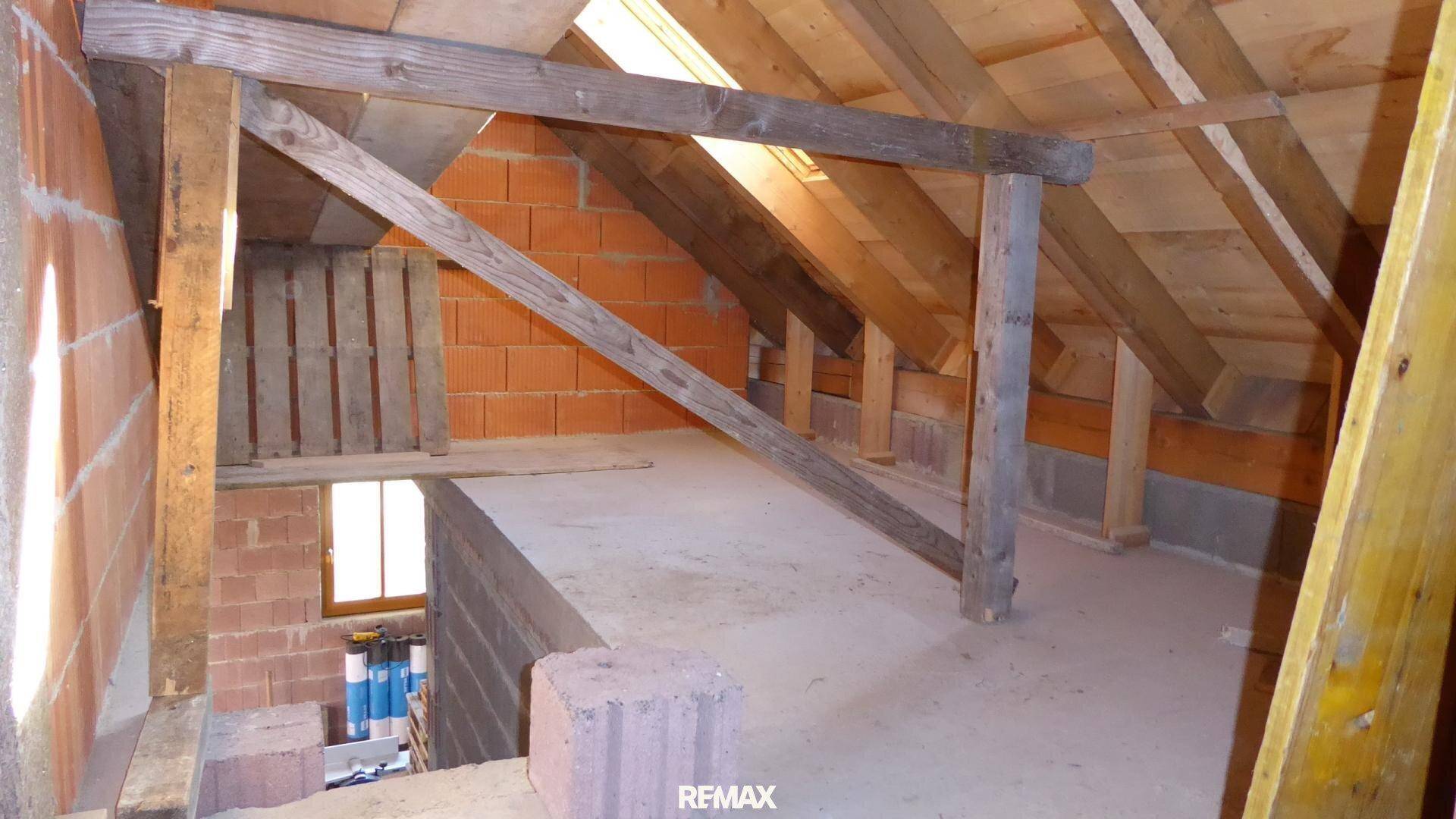Dachboden im Rohbau mit sichtbaren Holzbalken und Ziegelwänden, bereit für den Ausbau.