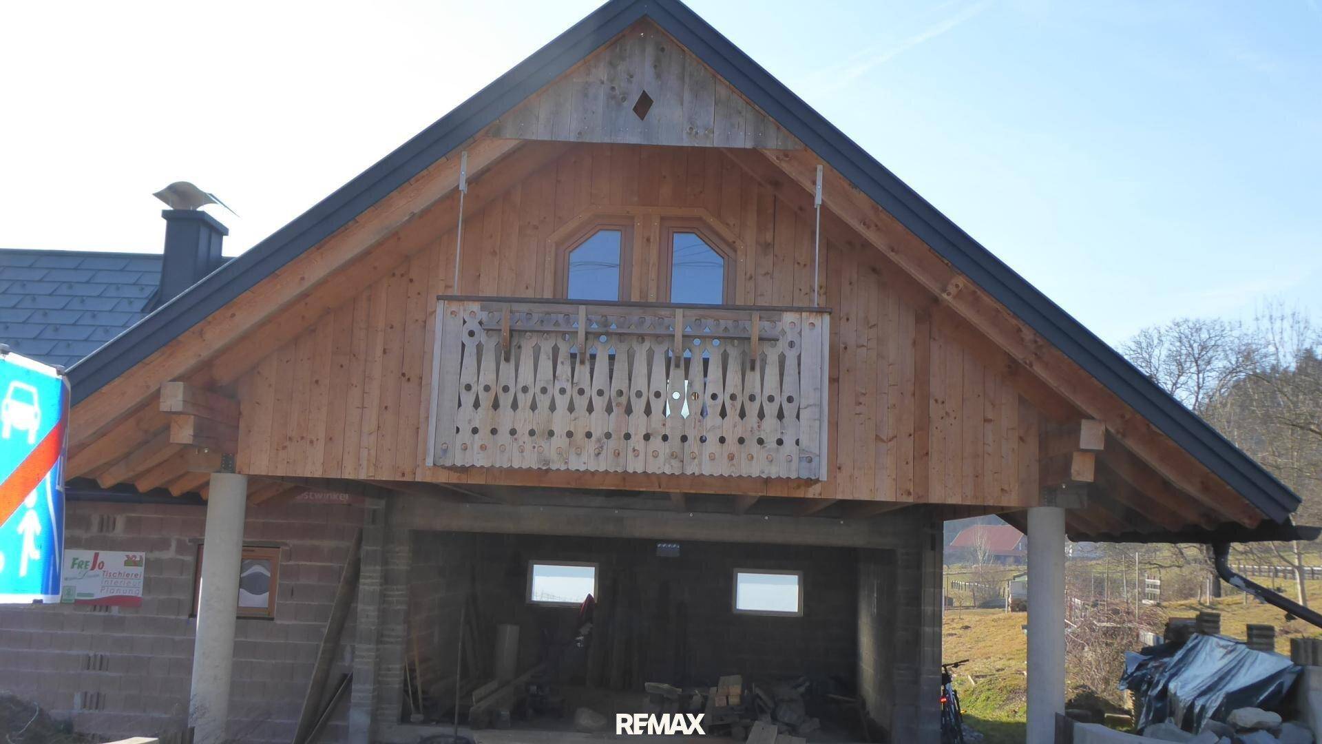 Frontansicht des Neubaus mit Holzverkleidung und traditionellem Holzbalkon.