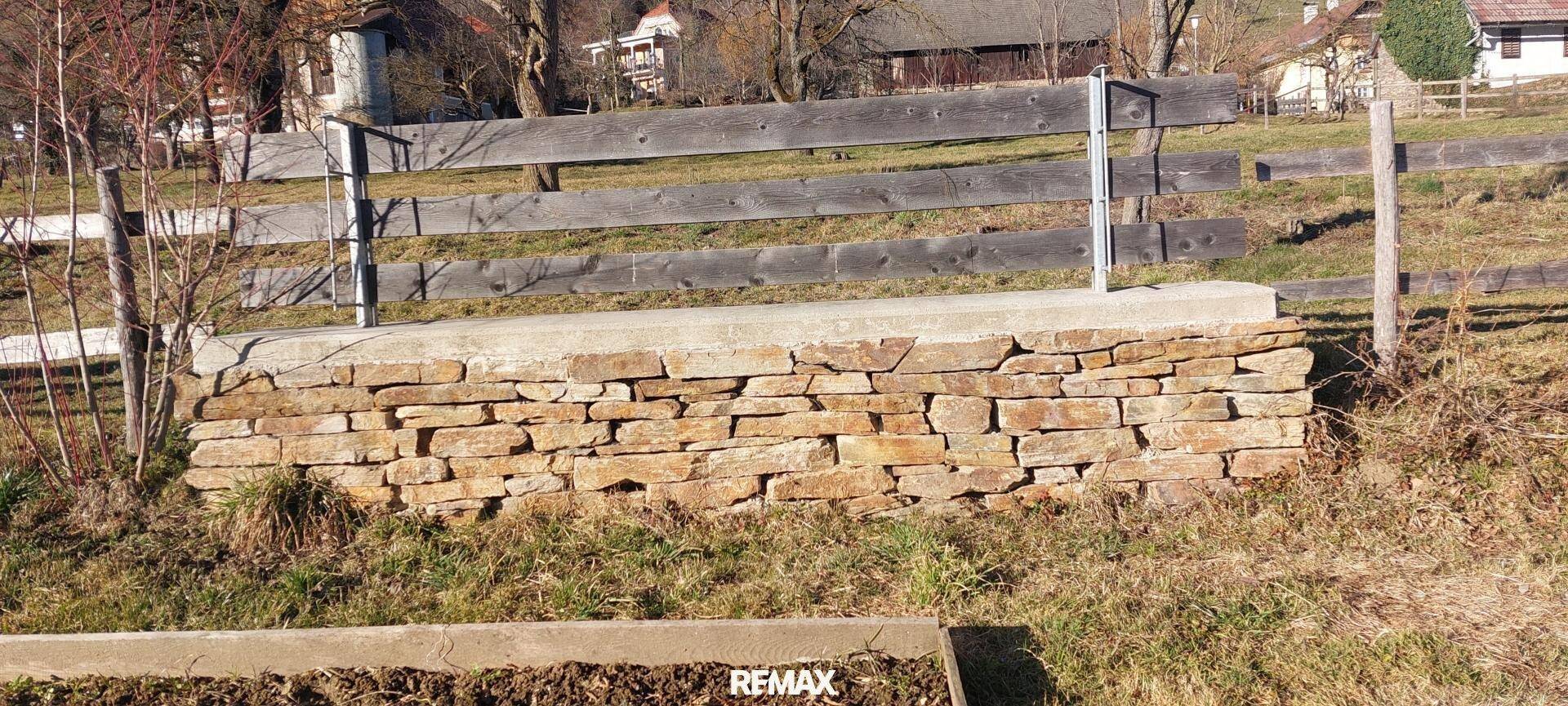 Natursteinmauer als Begrenzung im Gartenbereich, umgeben von Gras und Erde.