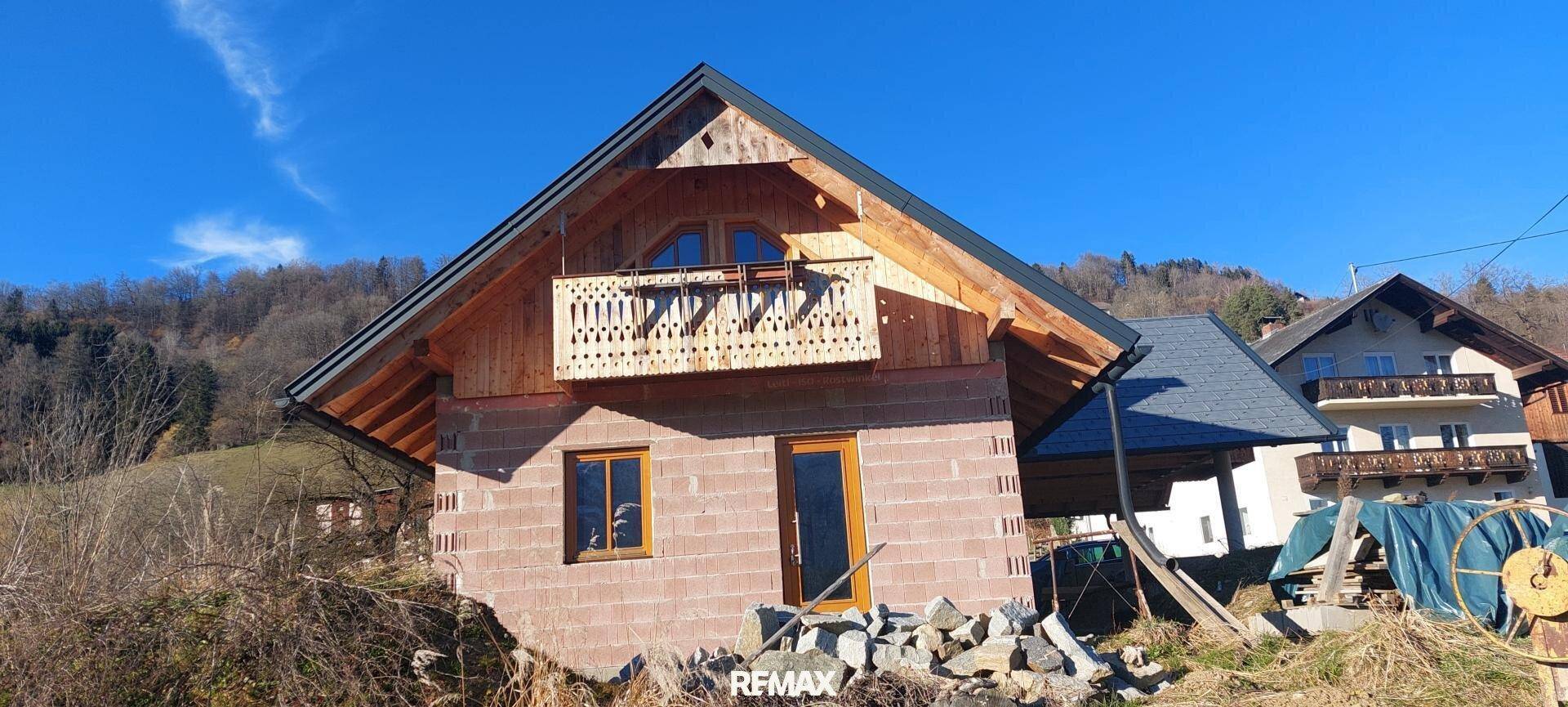 Vorderansicht des im Bau befindlichen Hauses mit Holzbalkon und traditioneller Architektur.