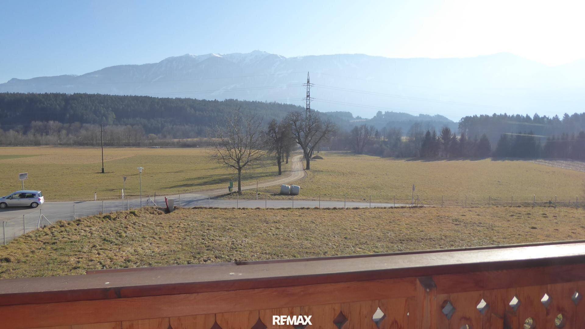 Weitläufiger Blick vom Balkon über Felder und eine Straße bis zu den fernen Bergen.