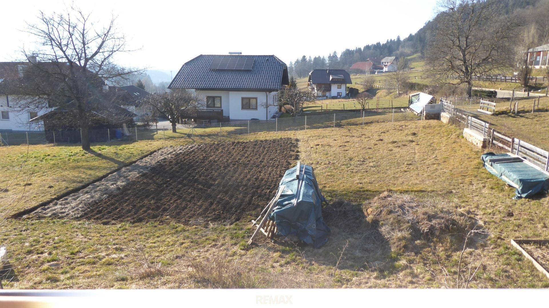 Gartenbereich mit vorbereitetem Beet und weiten Feldern im Hintergrund, umgeben von Natur.