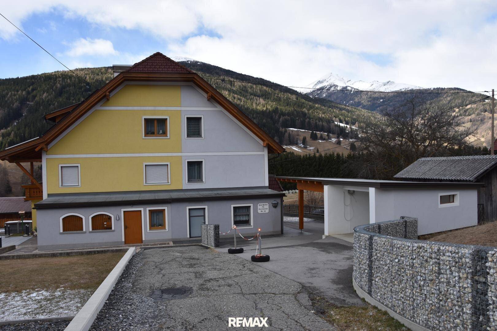 Traditionelles Haus mit gelber und grauer Fassade, umgeben von einer bergigen Landschaft.
