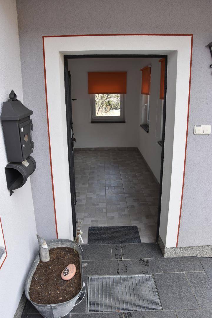 Eingangsbereich mit gefliestem Boden und Blick in einen leeren Raum mit Fenster.