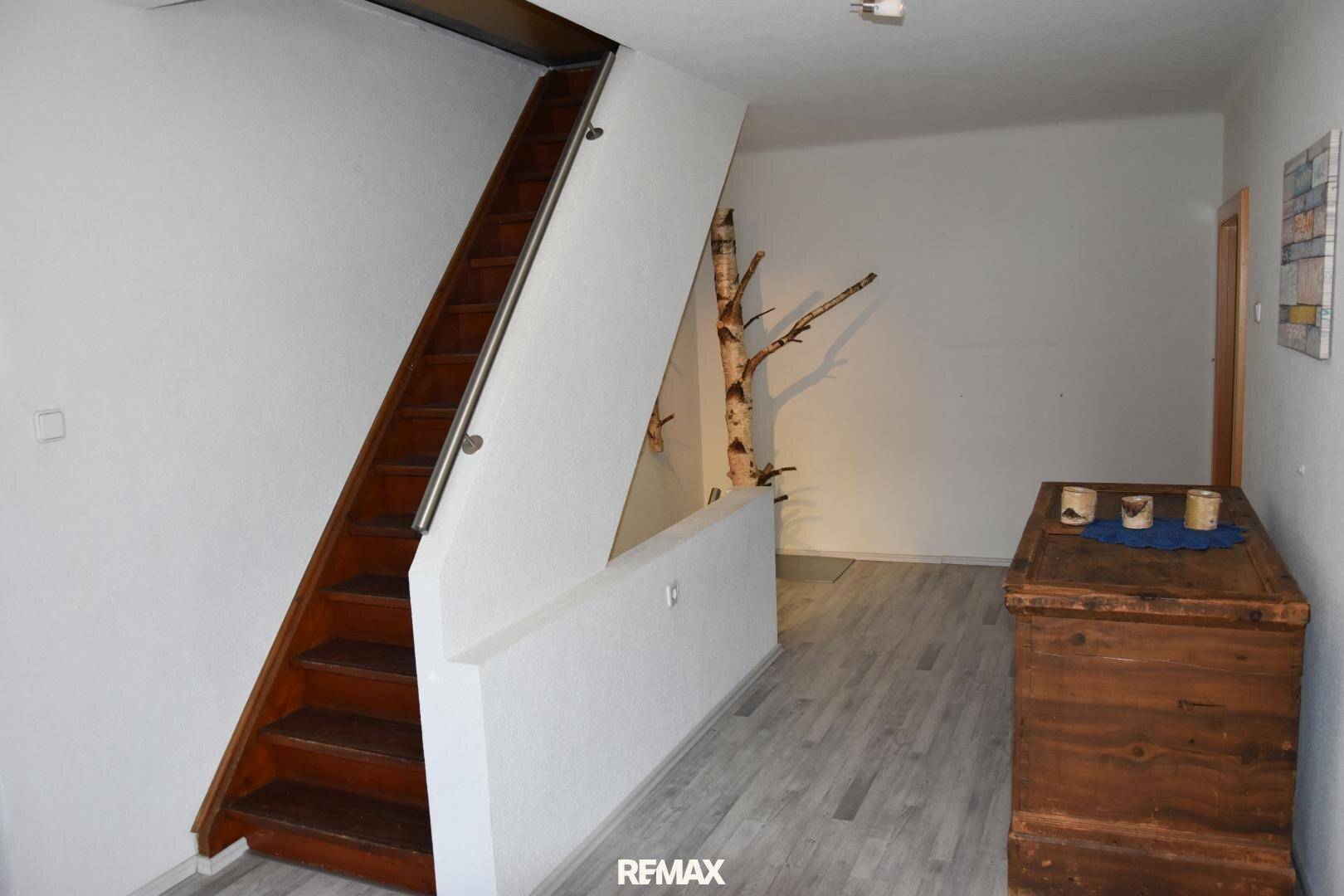 Heller Flur mit Holztreppe, modernem Bodenbelag und dekorativem Birkenstamm.