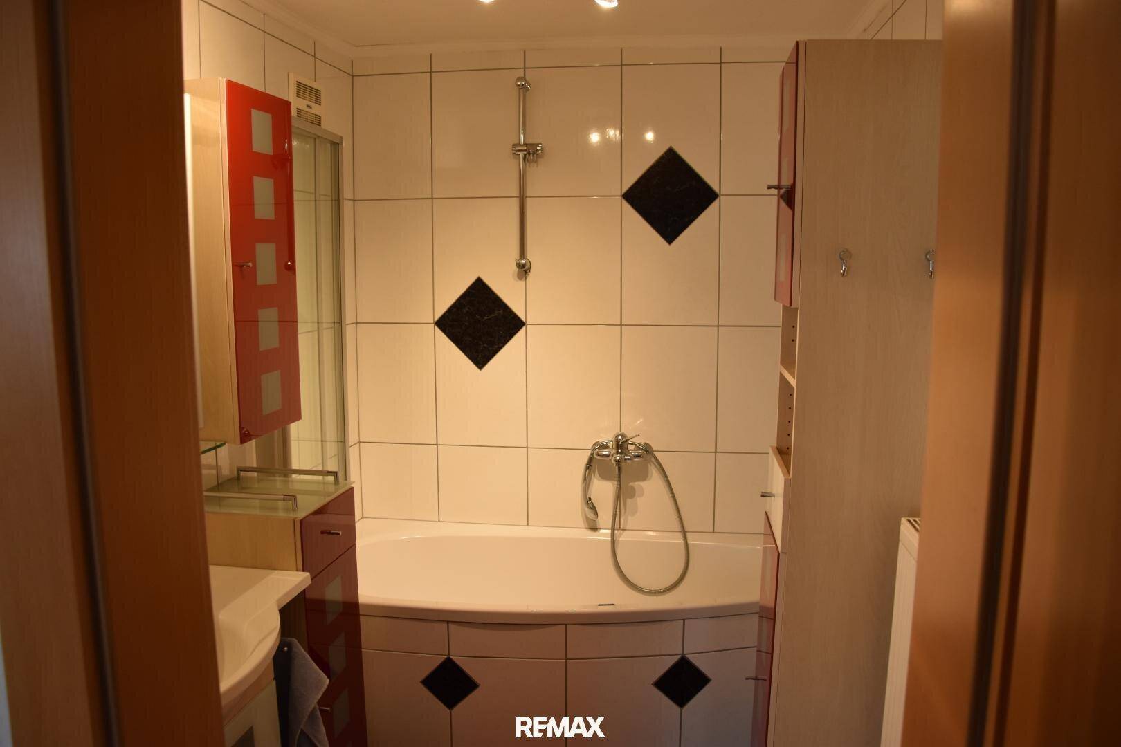 Badezimmer mit Badewanne, weißen Fliesen und roten Akzenten, funktional gestaltet.