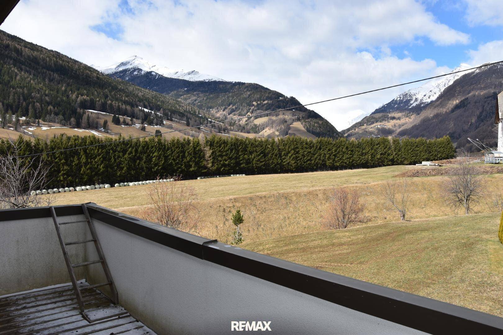 Balkon mit weitem Blick auf die umliegende Berglandschaft und grüne Wiesen.