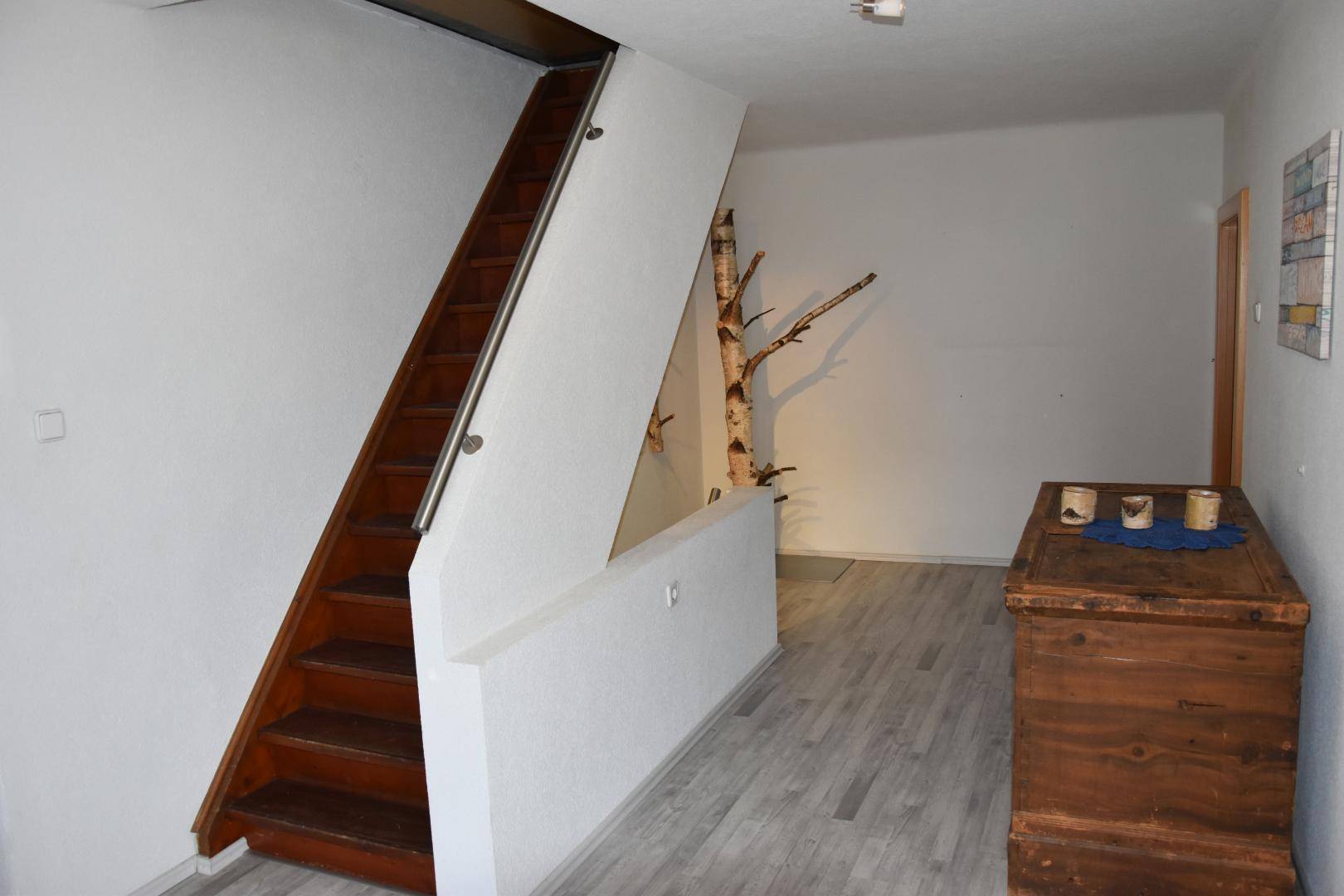 Heller Flur mit Holztreppe, modernem Laminatboden und dekorativem Birkenstamm.