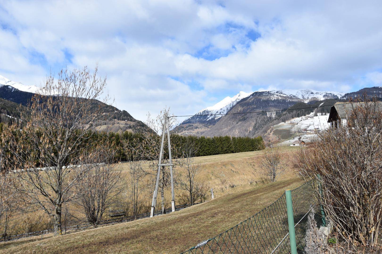 Weitläufige Landschaft mit grünen Wiesen, Bäumen und schneebedeckten Bergen im Hintergrund.