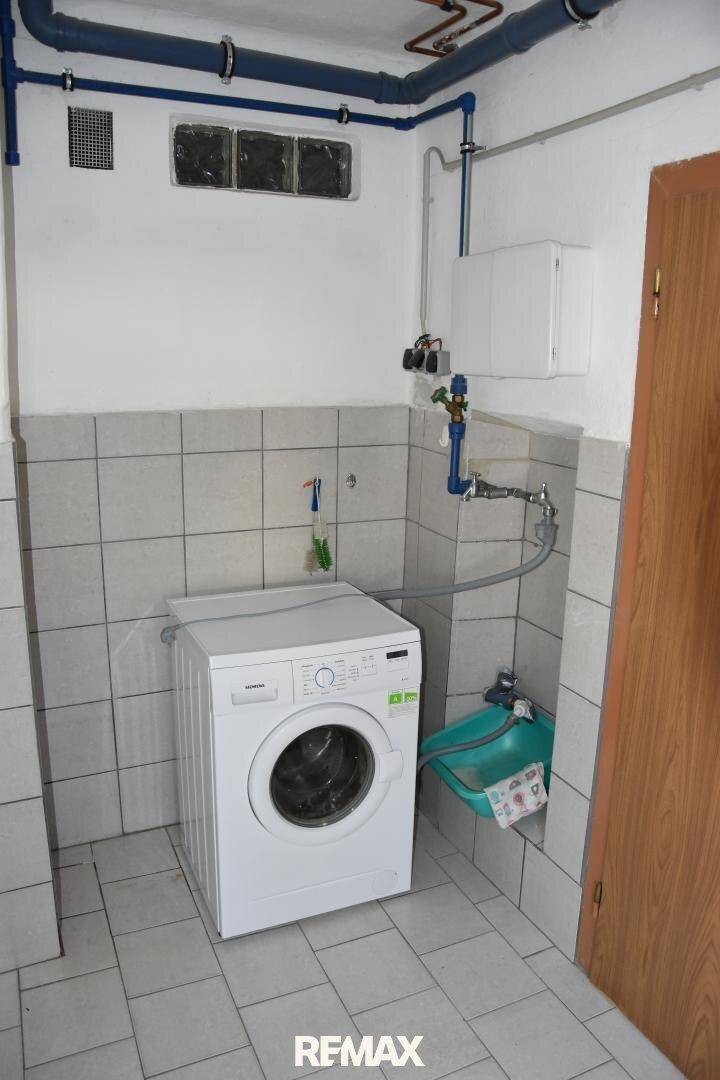 Hauswirtschaftsraum mit Waschmaschine, gefliestem Boden und sichtbaren Wasserleitungen.