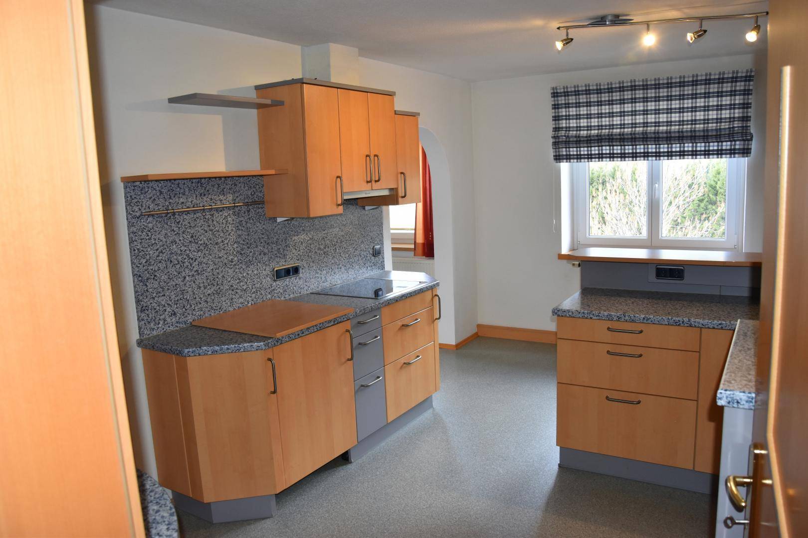 Funktionale Küche mit Holzschränken, dunklen Arbeitsplatten und integrierten Geräten.