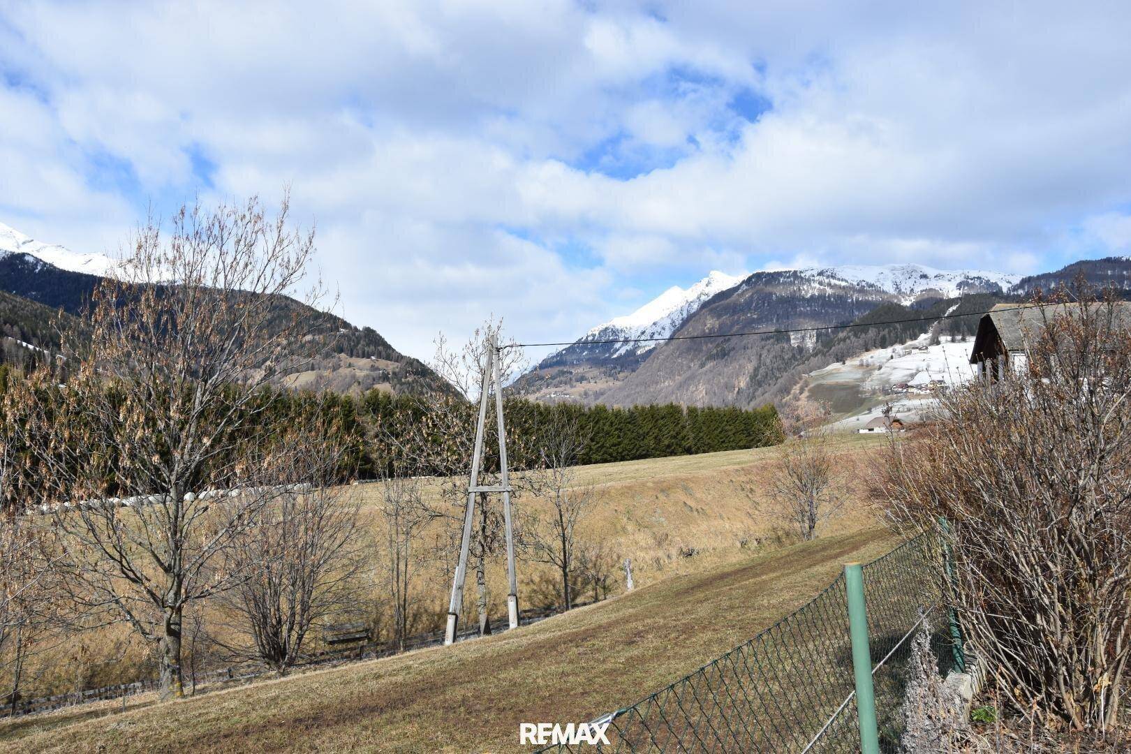 Weitläufiger Blick auf die schneebedeckten Berge und grüne Wiesen in der Umgebung.