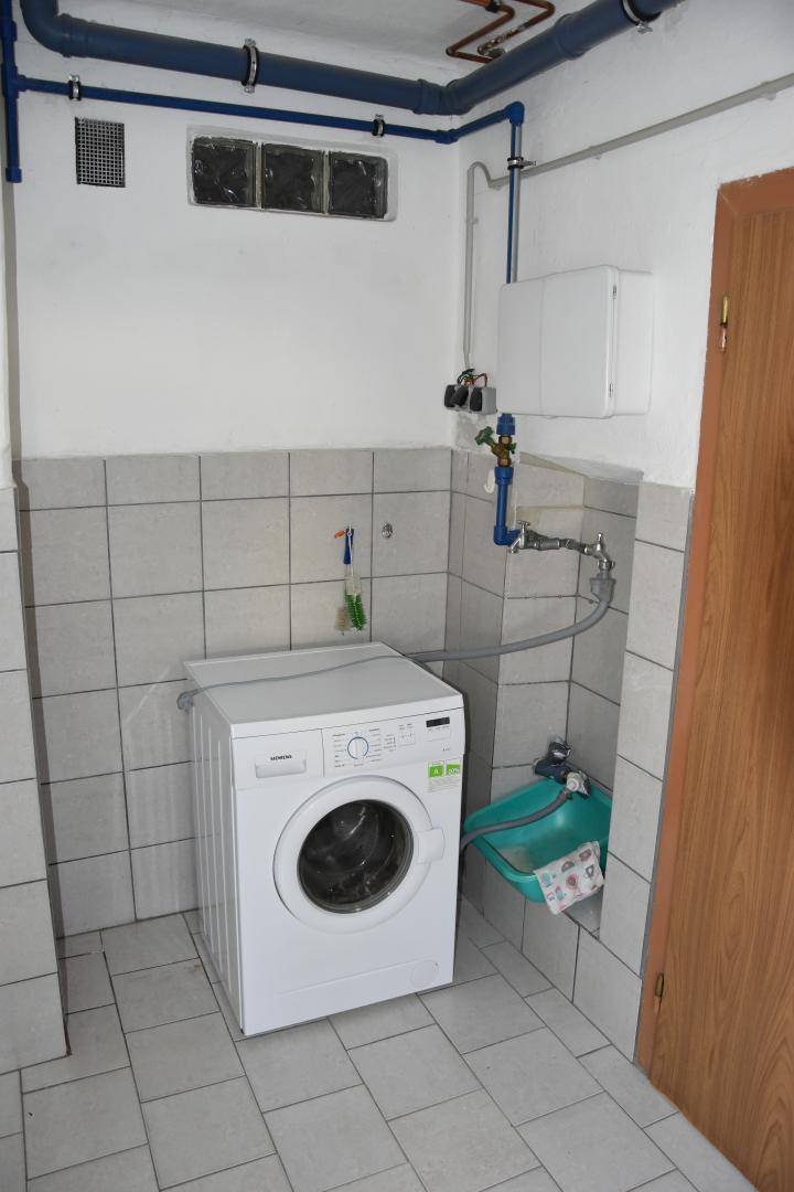 Hauswirtschaftsraum mit Waschmaschine, Fliesenboden und sichtbaren Wasserleitungen.