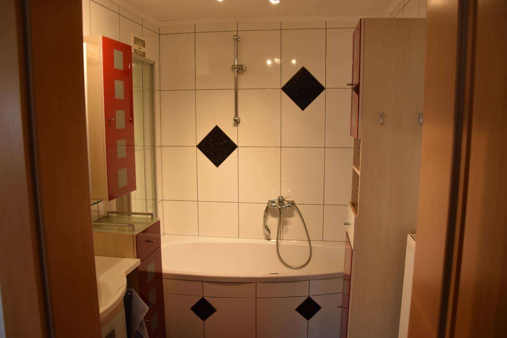 Badezimmer mit Eckbadewanne, weißen Fliesen und schwarzen Dekorelementen.