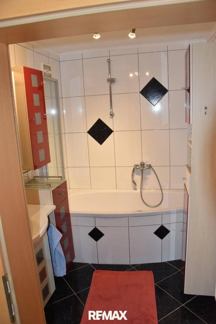 Modernes Badezimmer mit Badewanne, Duschfunktion und stilvollen schwarzen Akzentfliesen.
