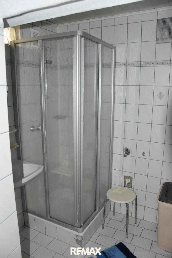 Kleines Badezimmer mit Duschkabine und weißen Fliesen, funktional eingerichtet.