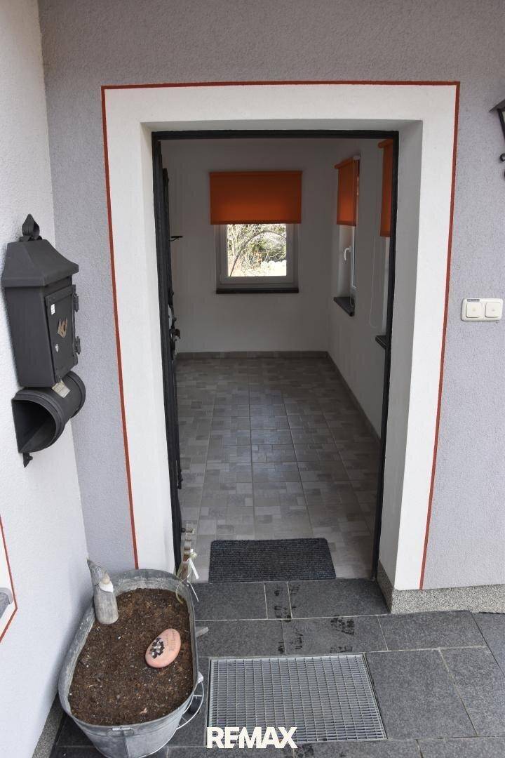 Eingangsbereich mit gefliestem Boden und einem Fenster mit orangefarbenem Rollo.