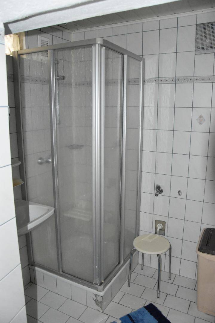 Badezimmer mit weiß gefliesten Wänden und einer Duschkabine in der Ecke.