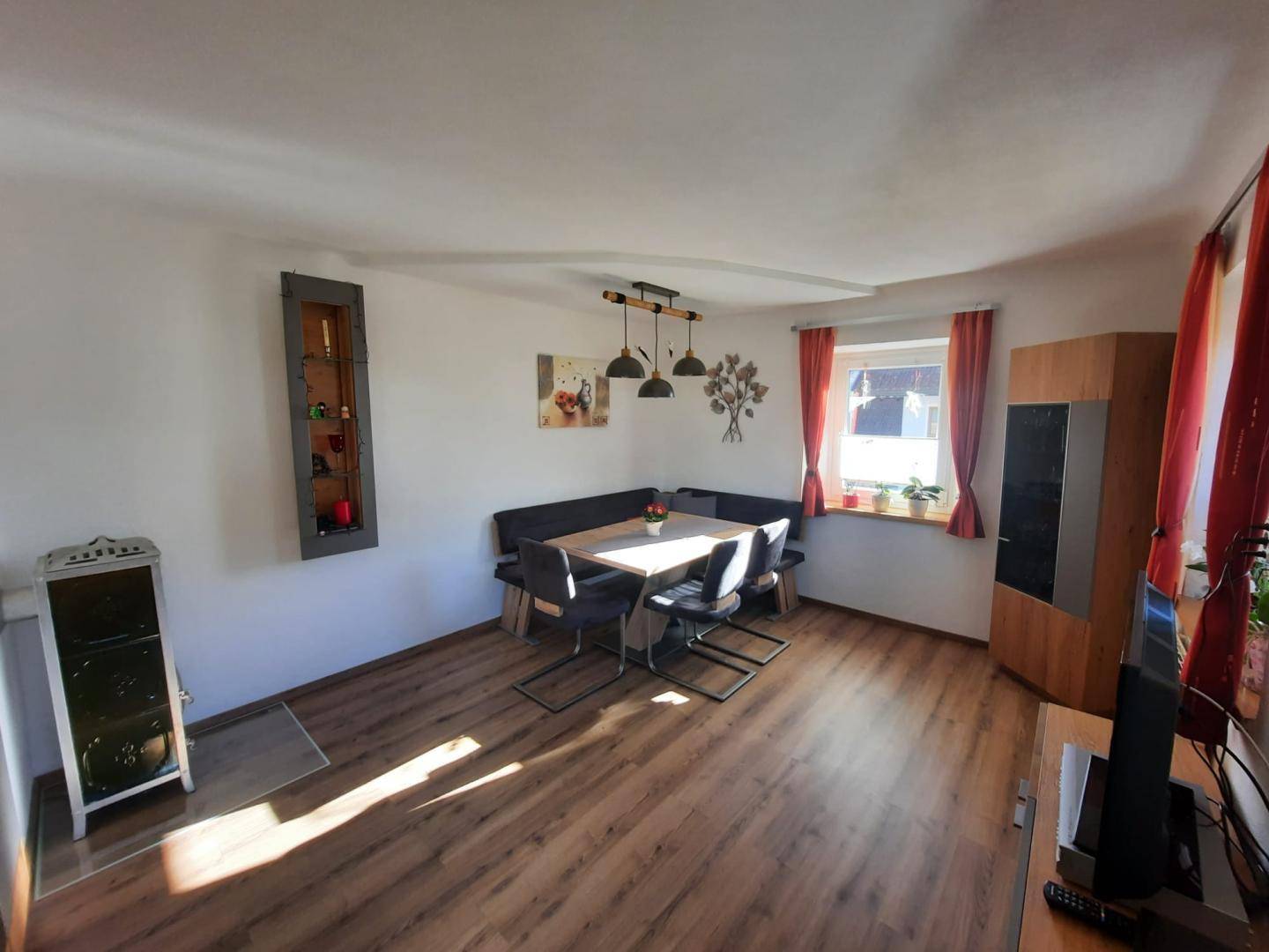 Gemütlicher Wohn-Essbereich mit Laminatboden, Eckbank und einem Kaminofen.