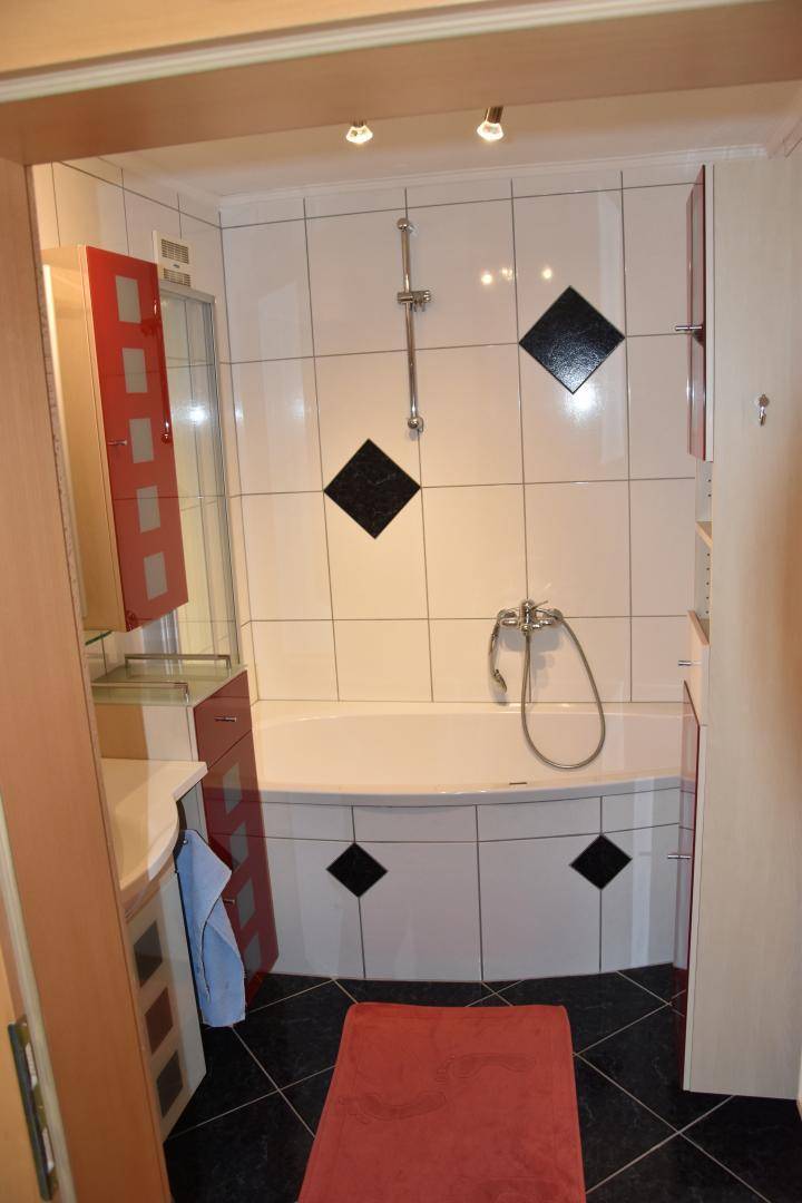 Modernes Badezimmer mit Eckbadewanne, weißen Fliesen und roten Akzenten.