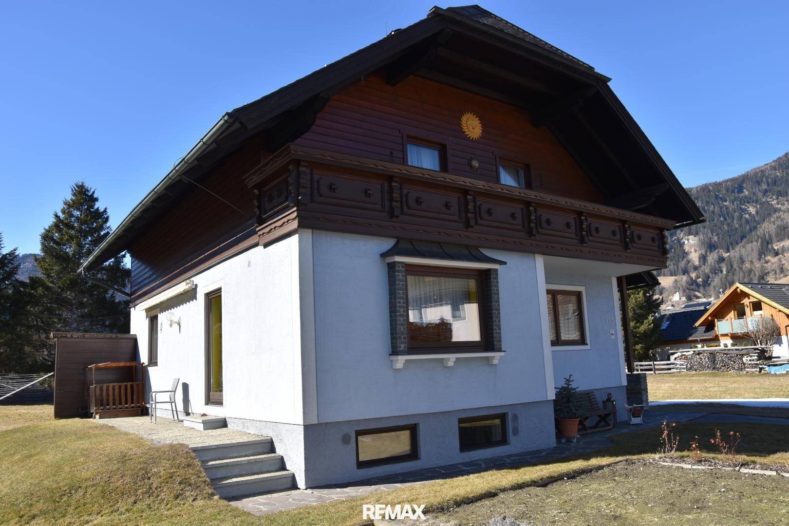 Traditionelles Haus mit Holzbalkon und gepflegtem Gartenbereich in alpiner Umgebung.