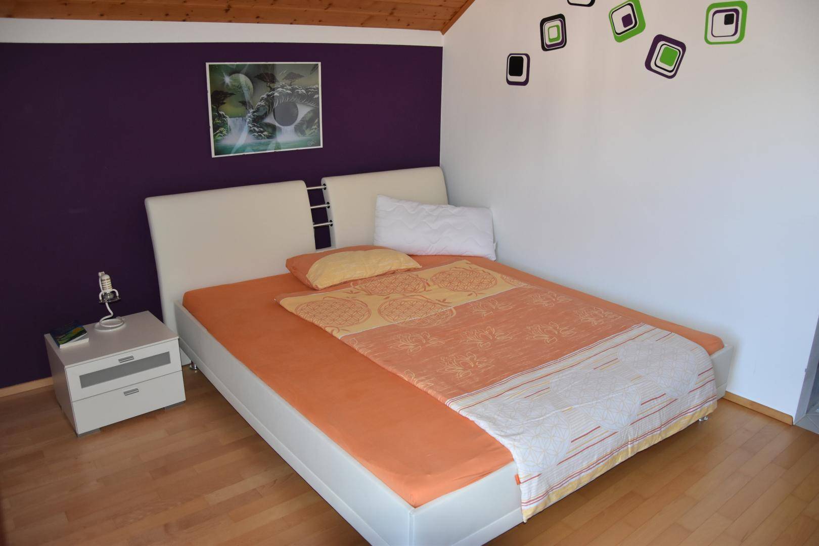 Schlafzimmer mit Doppelbett, weißem Bettrahmen und lila Akzentwand.