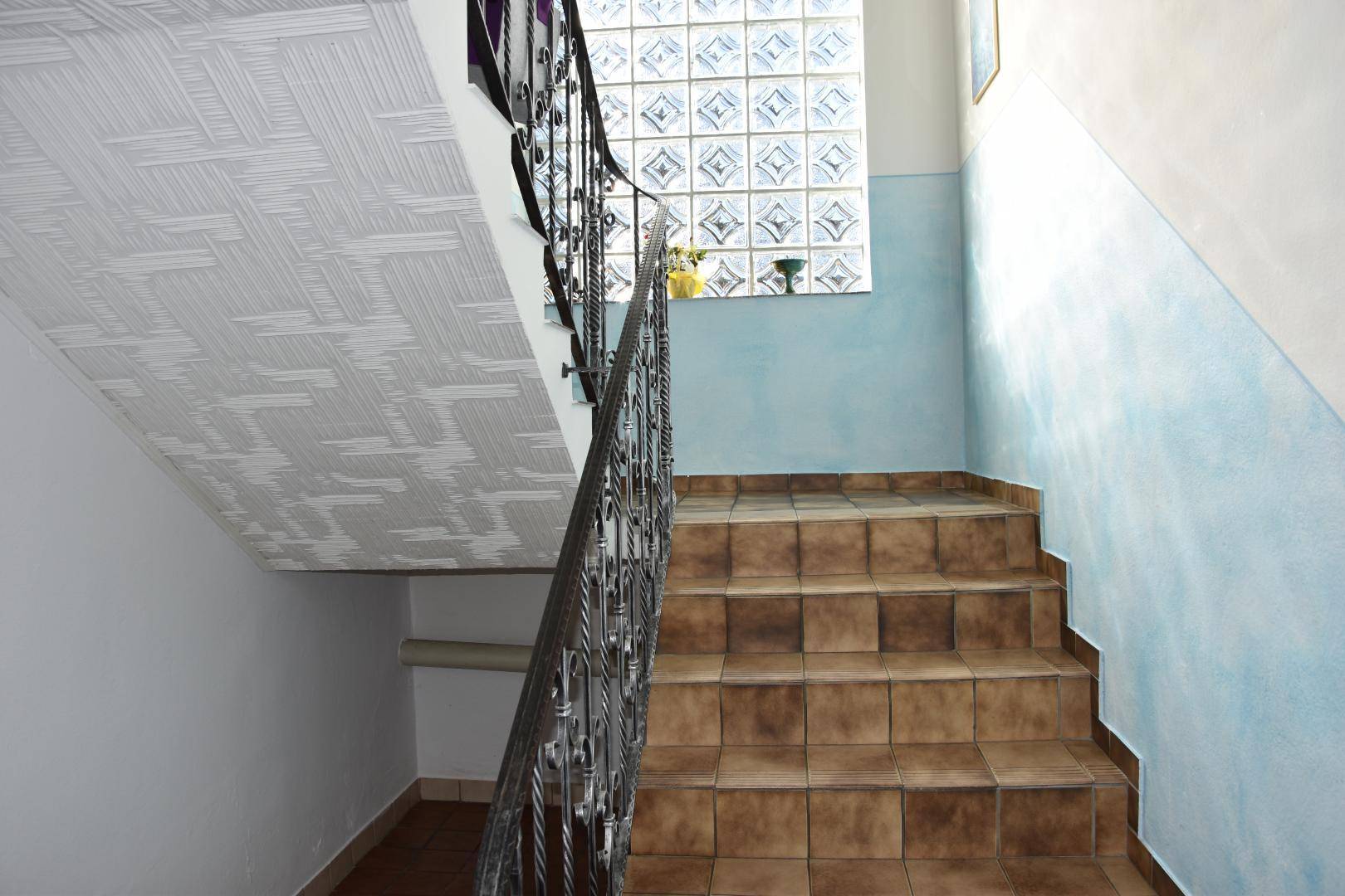 Treppenhaus mit gefliesten Stufen und schmiedeeisernem Geländer, das in die obere Etage führt.