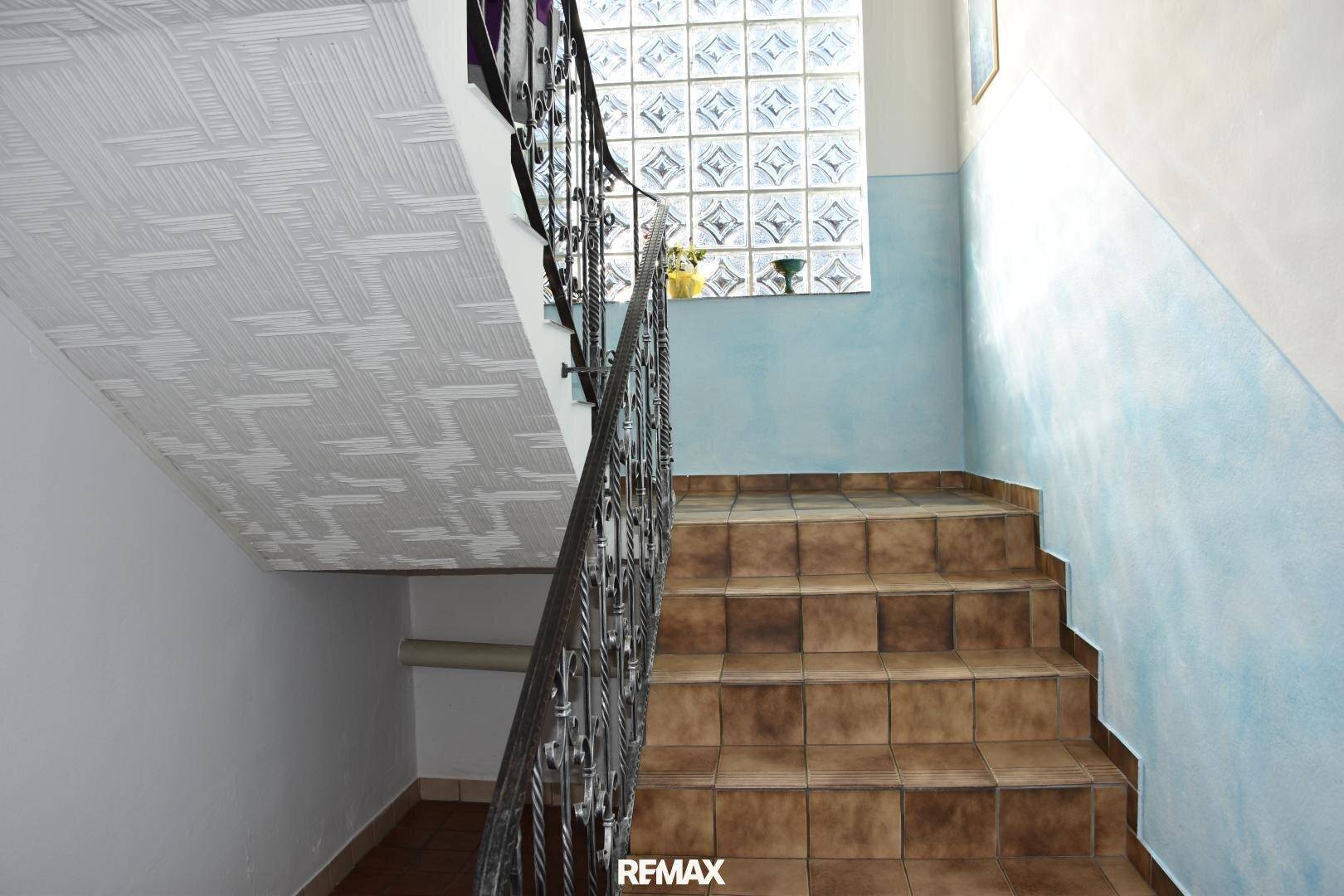 Treppenhaus mit Fliesenstufen, schmiedeeisernem Geländer und Glasbausteinwand.
