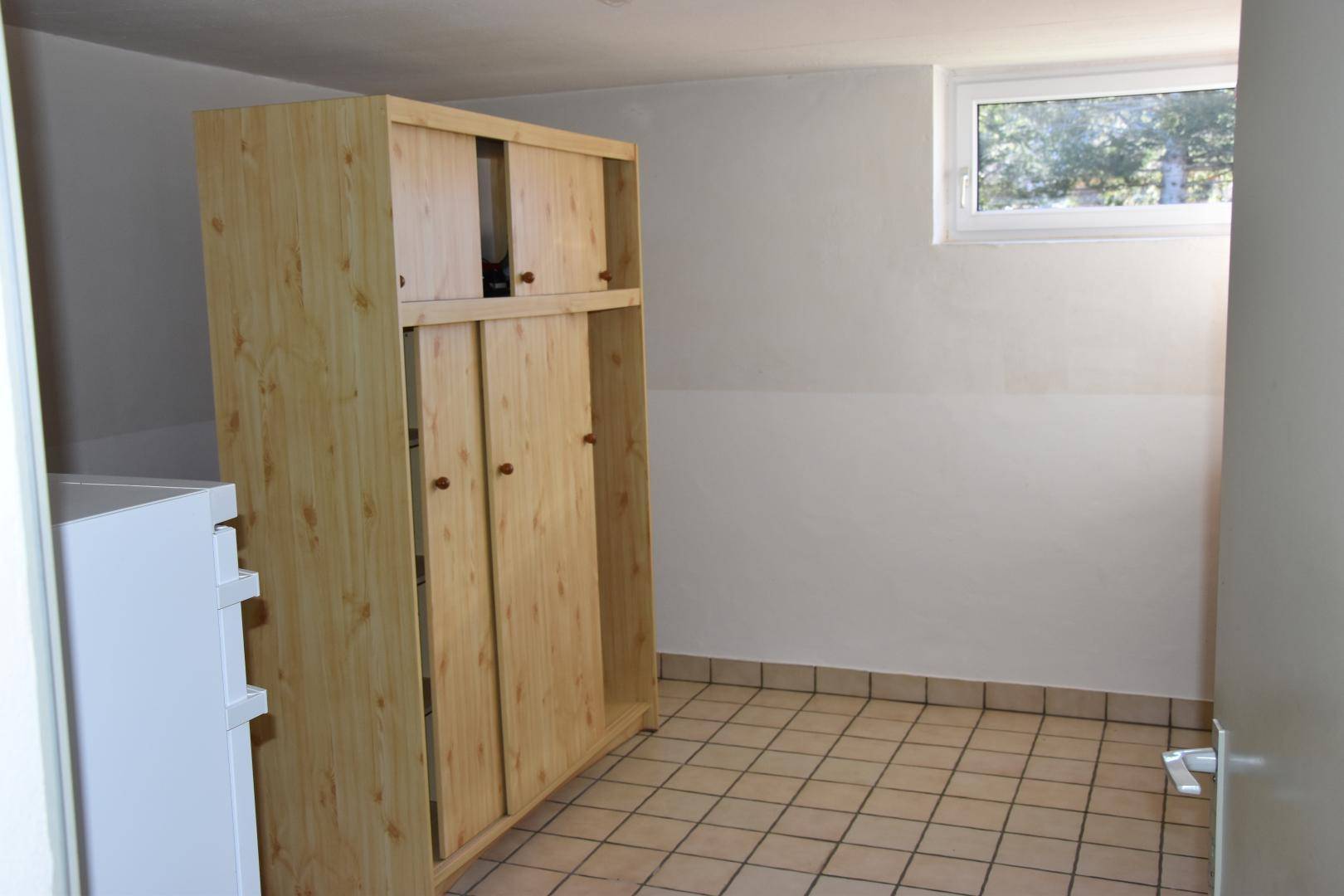 Abstellraum mit Holzschrank, gefliestem Boden und kleinem Fenster.