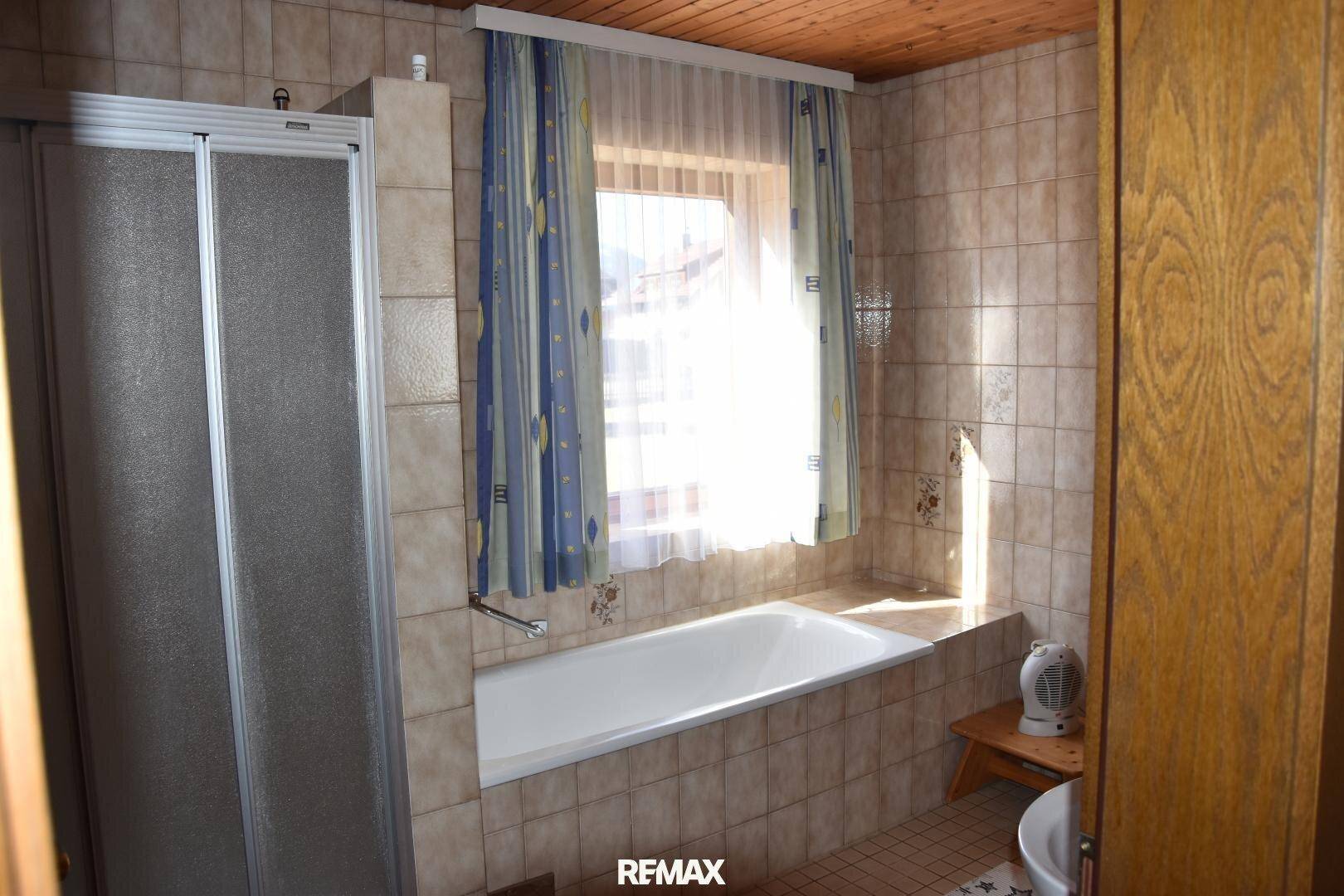 Helles Badezimmer mit Badewanne, Duschkabine und Fenster, gefliest in warmen Tönen.
