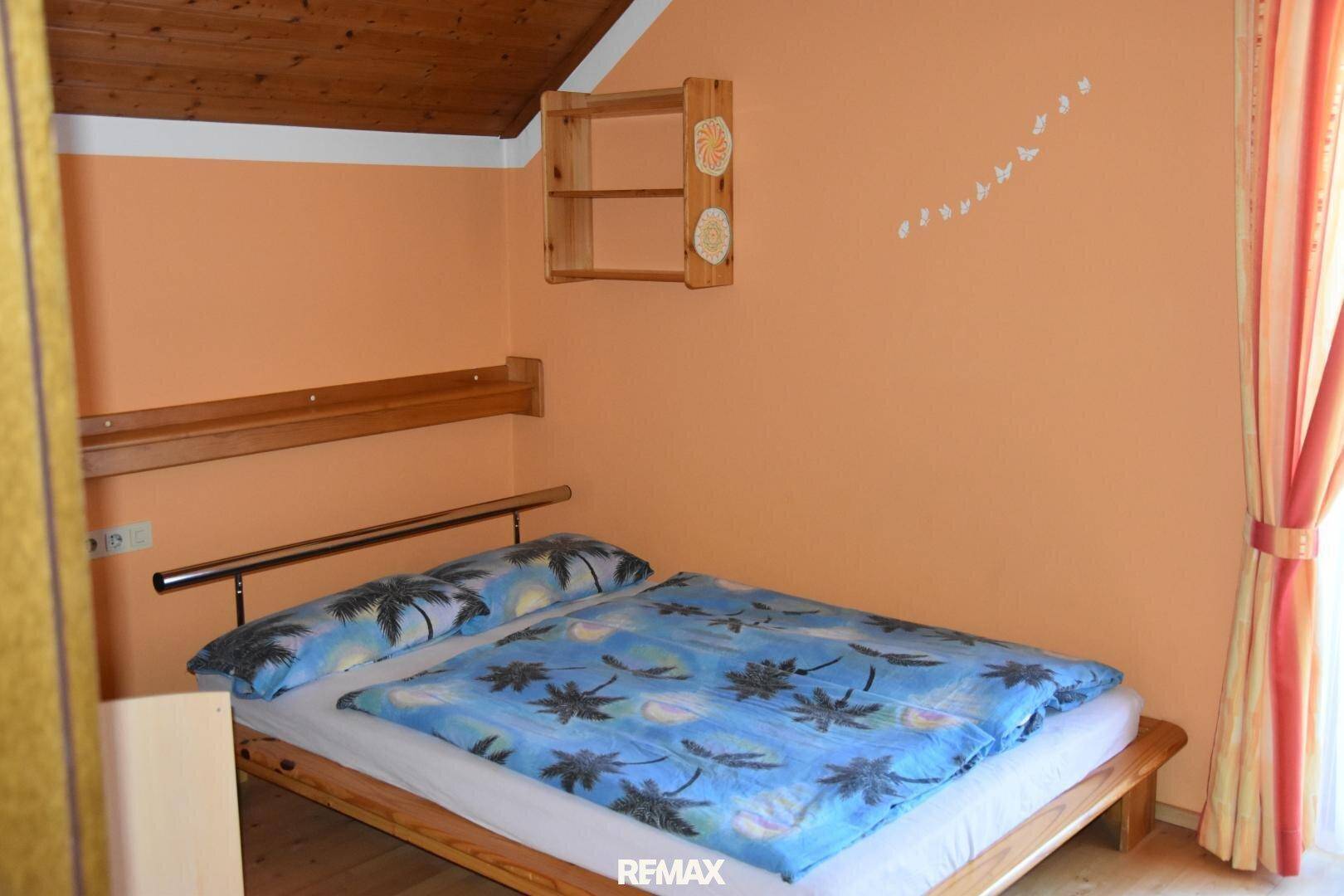 Schlafzimmer mit Einzelbett, orangefarbenen Wänden und Holzregal, hell und freundlich.